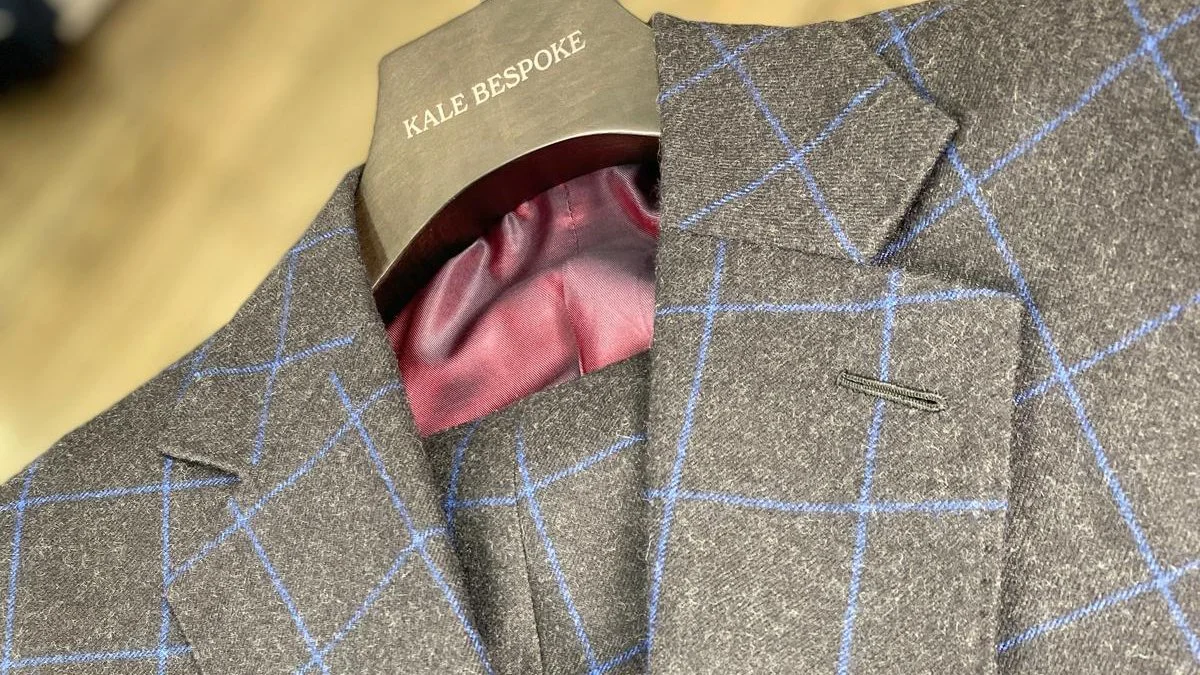 Close-up of a brown wool blazer with blue windowpane pattern, showing inside pink lining, displayed on a rack.
