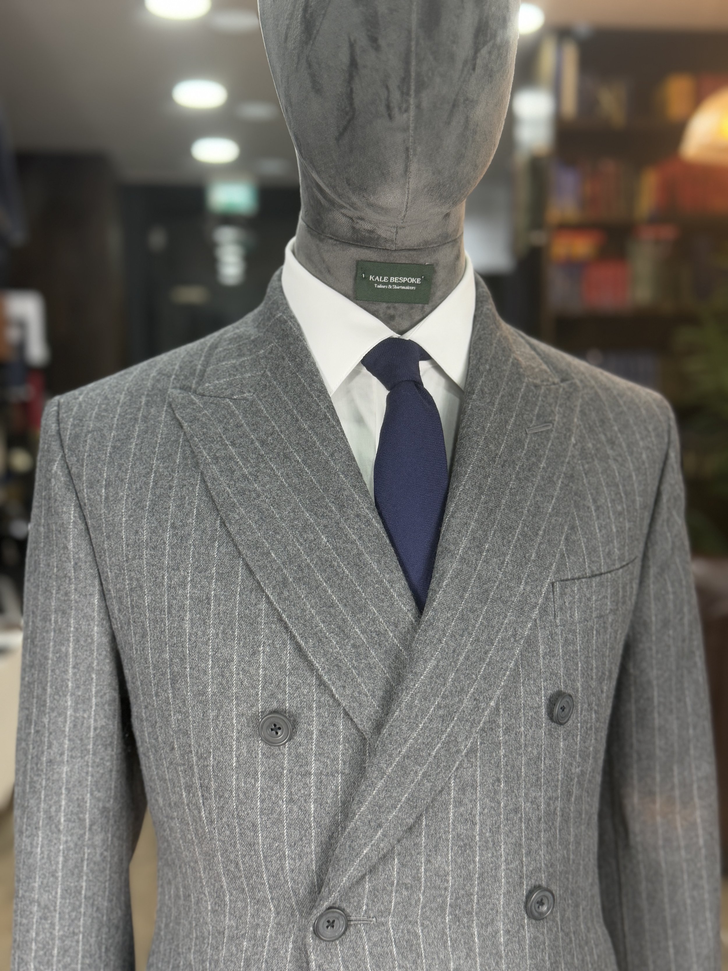Gray pinstripe double-breasted suit with white shirt and navy tie on a mannequin in a store.