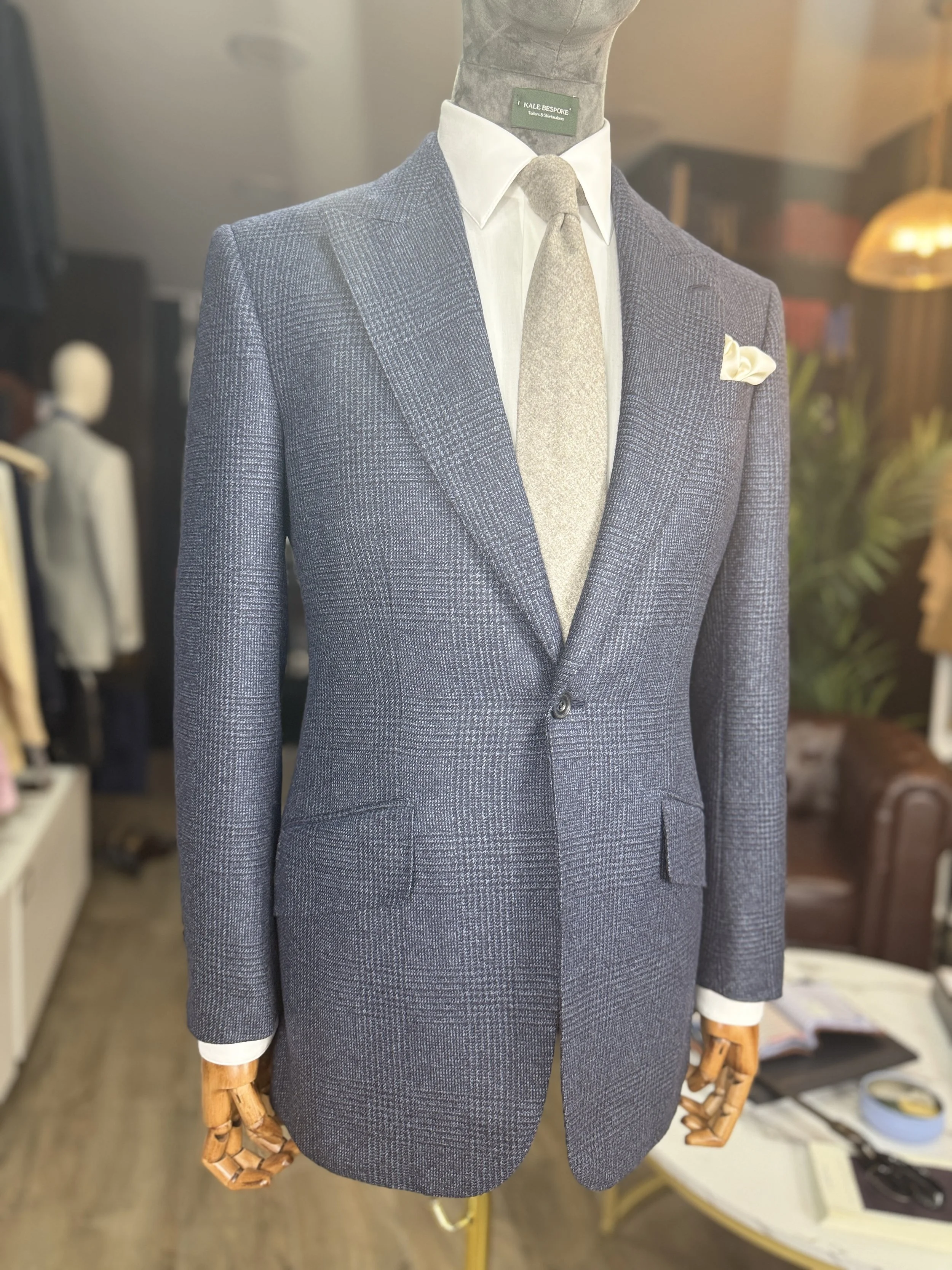 A mannequin dressed in a blue checkered suit with a white dress shirt, a light gray tie, a cream pocket square, in a clothing store.
