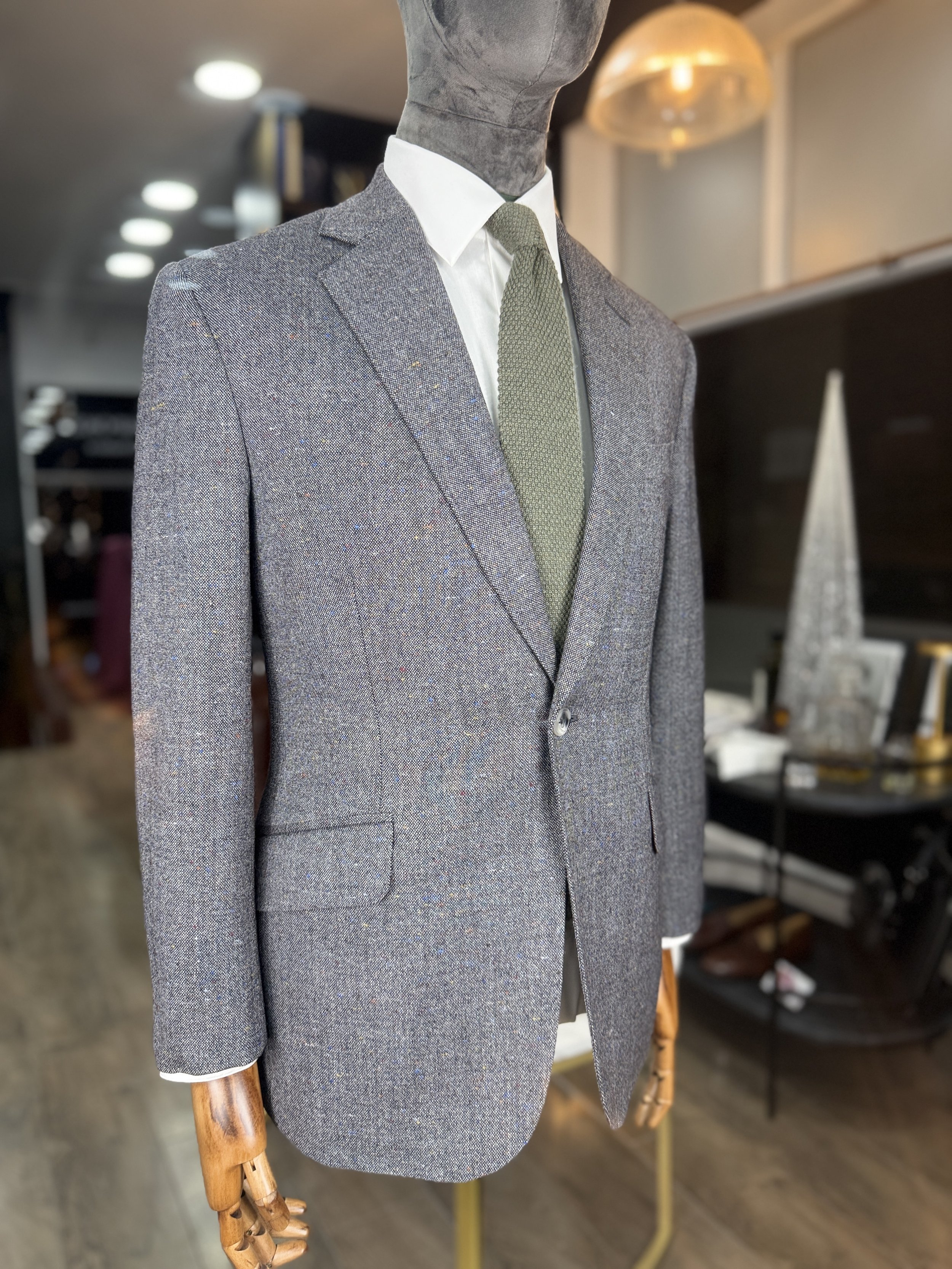 Gray tailored blazer suit on mannequin with white shirt and green tie in store setting.