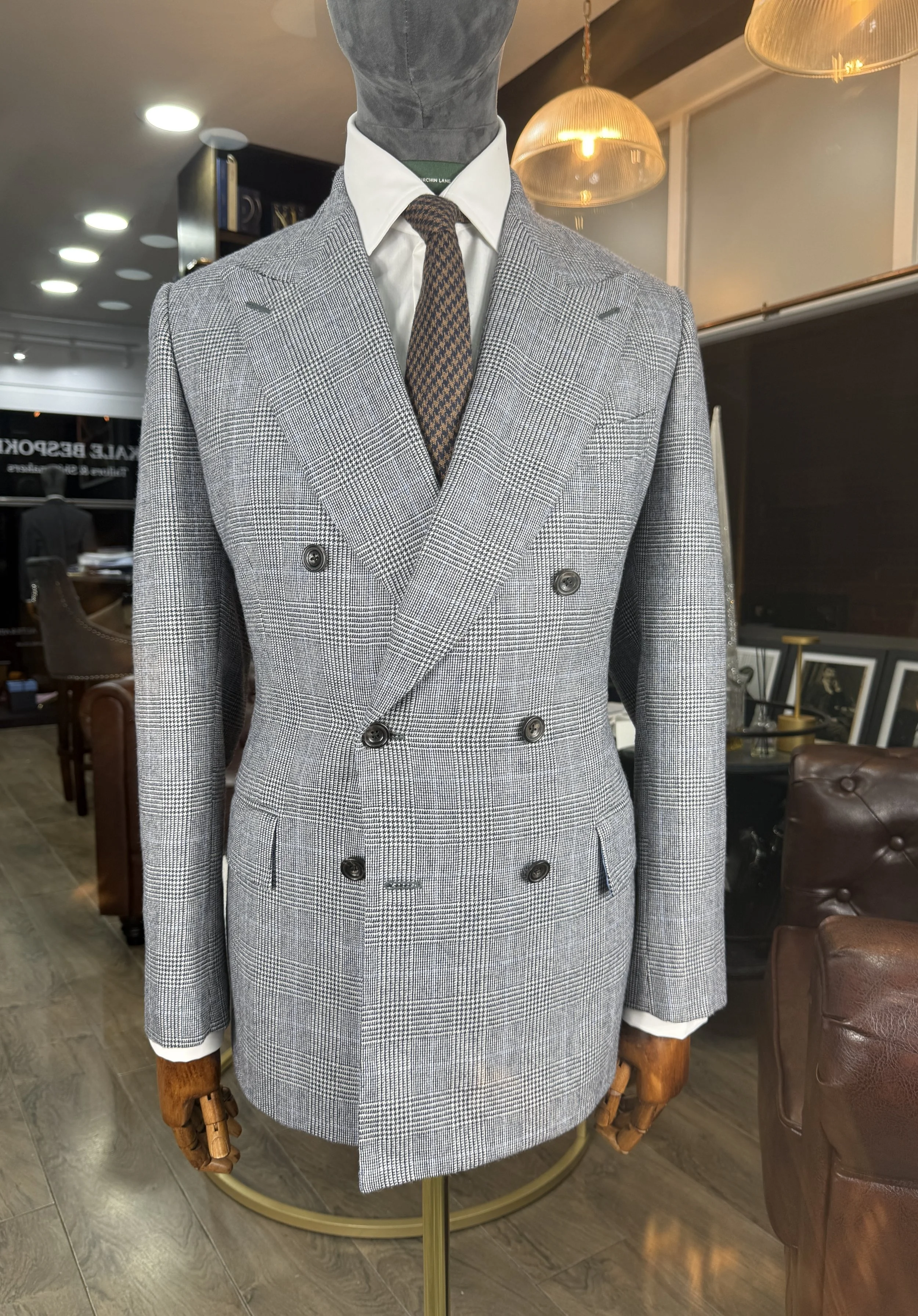 A mannequin wearing a double-breasted grey plaid suit with a white dress shirt and a brown patterned tie, displayed in a retail store.