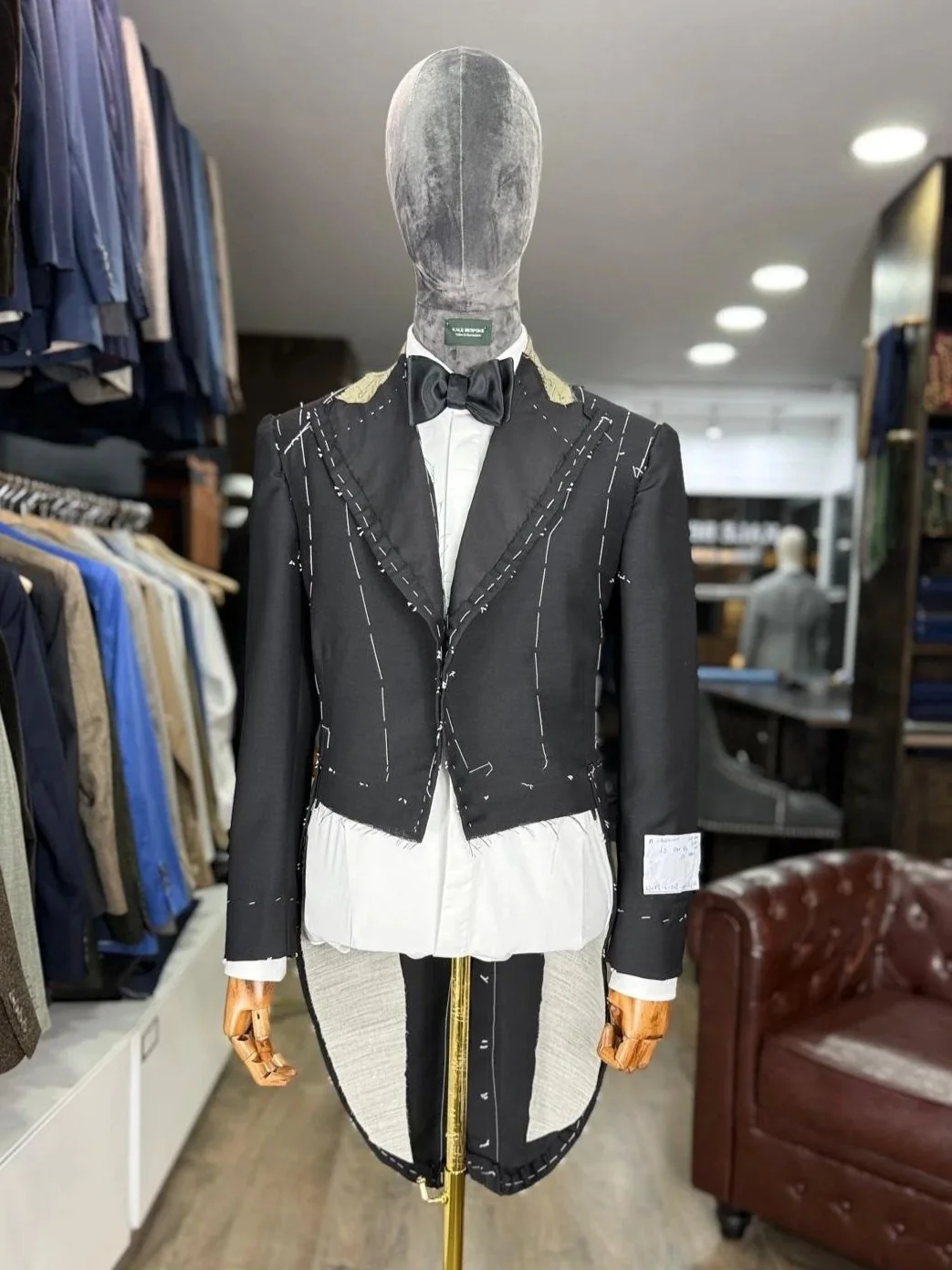 A mannequin dressed in a black blazer with sketch marks, a white shirt with a ruffled hem, a black bow tie, and an asymmetrical skirt with a zippers, displayed in a clothing store.
