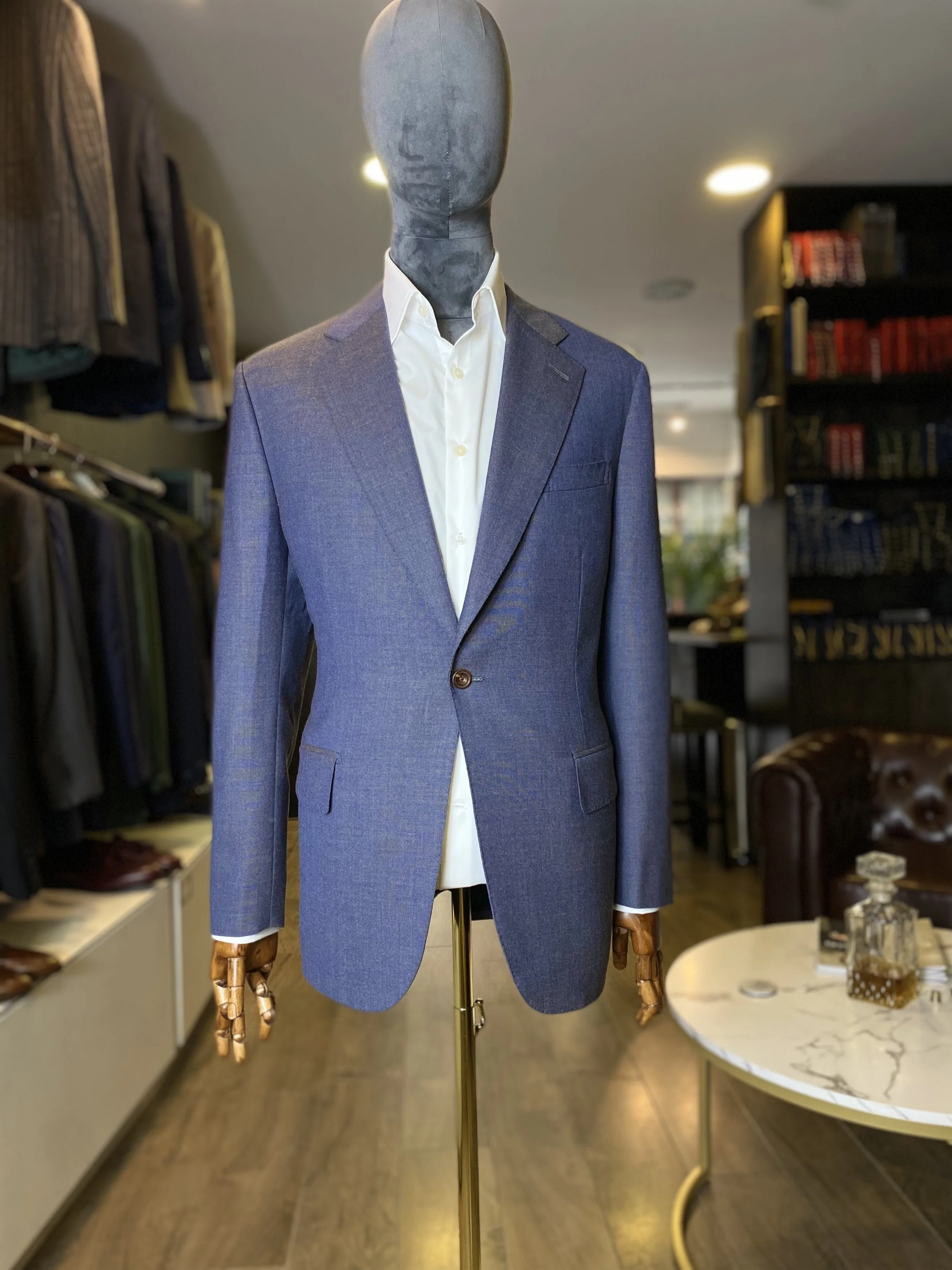 Blue/Grey Loro Piana High-twist Kale bespoke blazer. A sophisticated blue-grey one-button and slanted pockets blazer crafted from luxurious Loro Piana high twist wool, featuring elegant slanted pockets and a clean bespoke silhouette. Displayed on a s