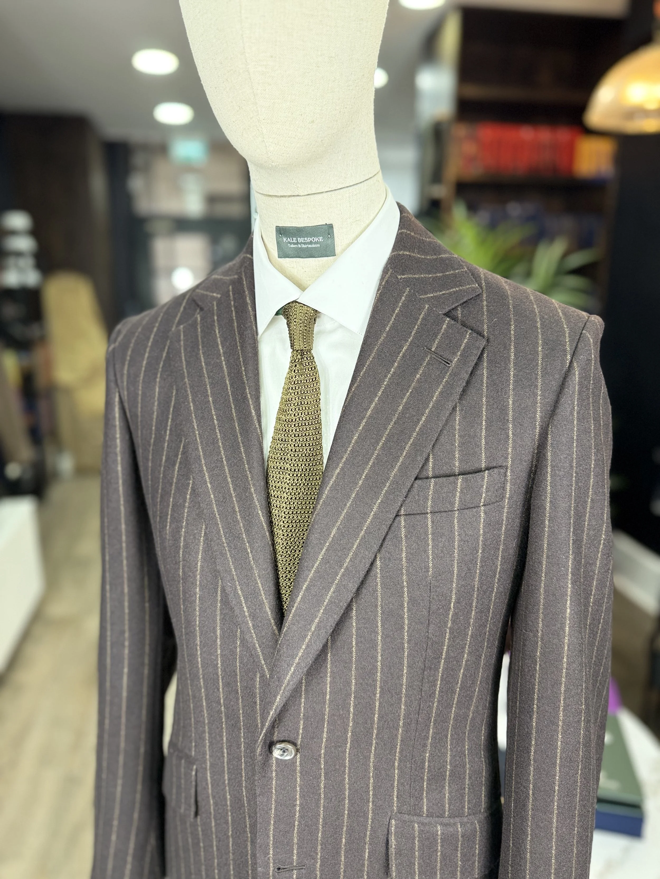 Brown flannel chalk stripe suit from standeven uxbridge flannel bunch 12oz.Two piece bespoke suit by Kale bespoke showcase on shop mannequin with green silk knitted tie.