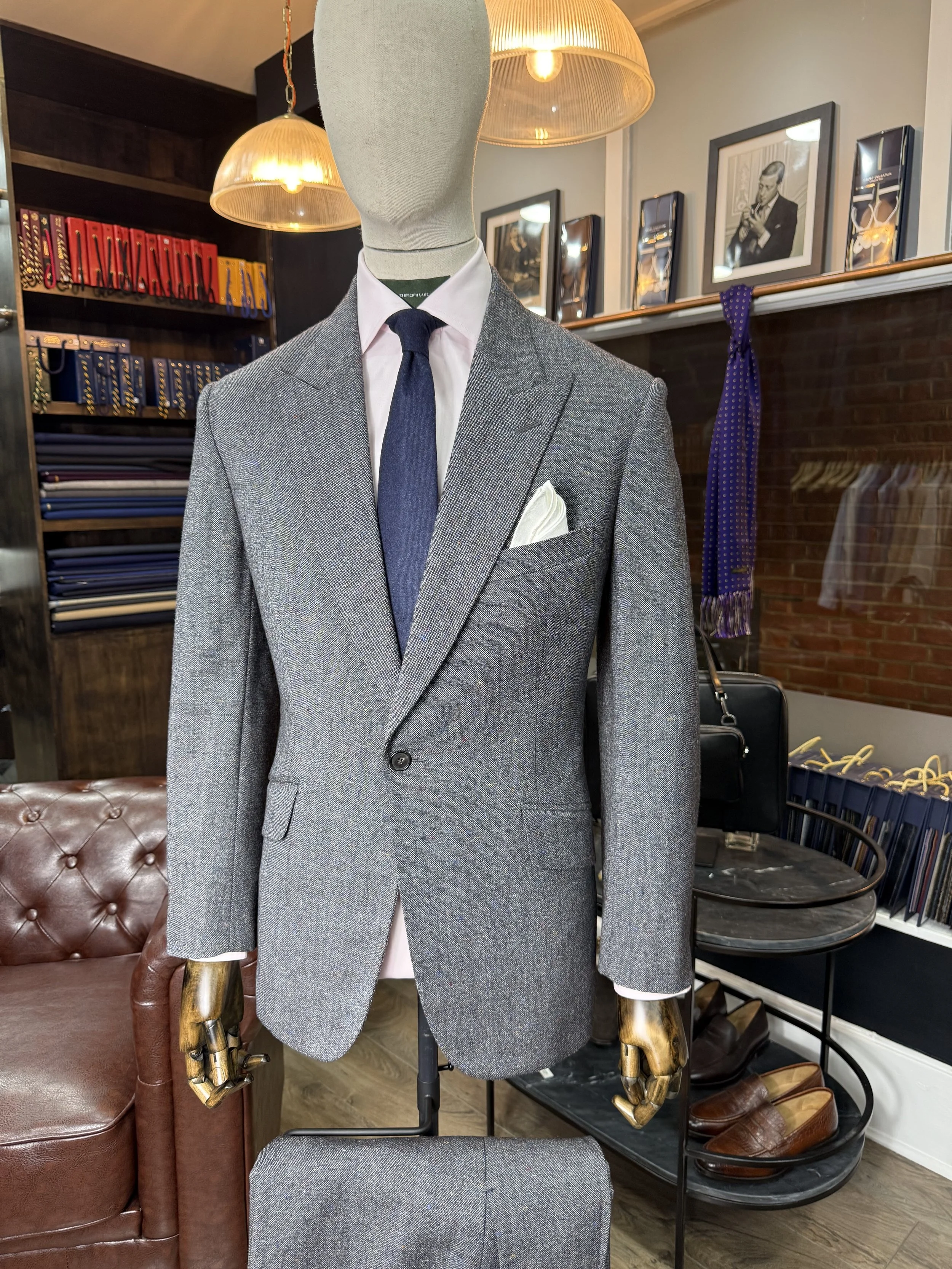 A mannequin dressed in a gray suit with a white shirt, a navy tie, a white pocket square, inside a clothing store.