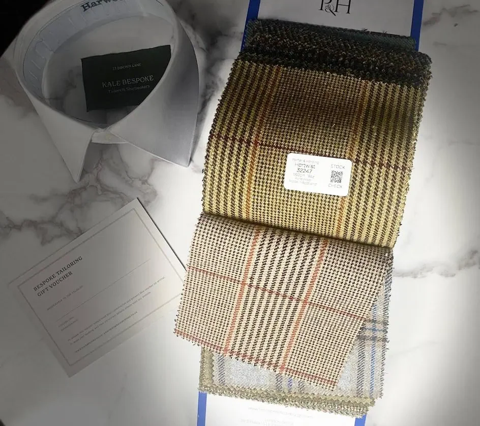 Display of fabric samples, a white collar shirt, a gift voucher, a drink, and a blue box.