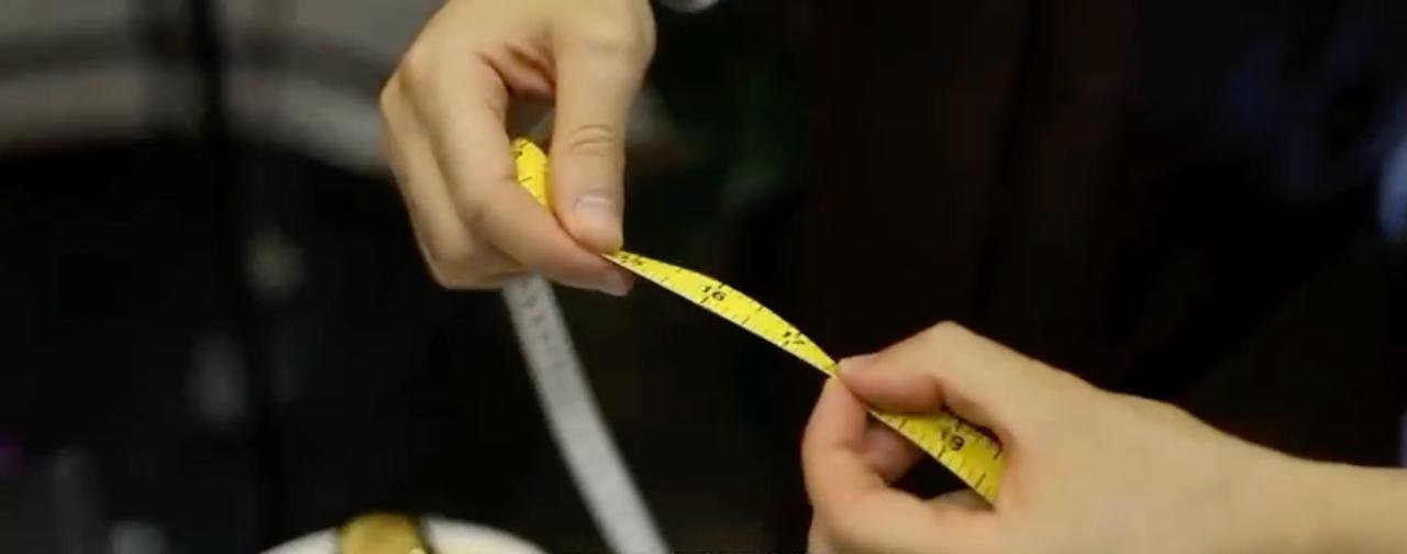 Close-up of two hands holding a yellow measuring tape, measuring an object or person's body part.