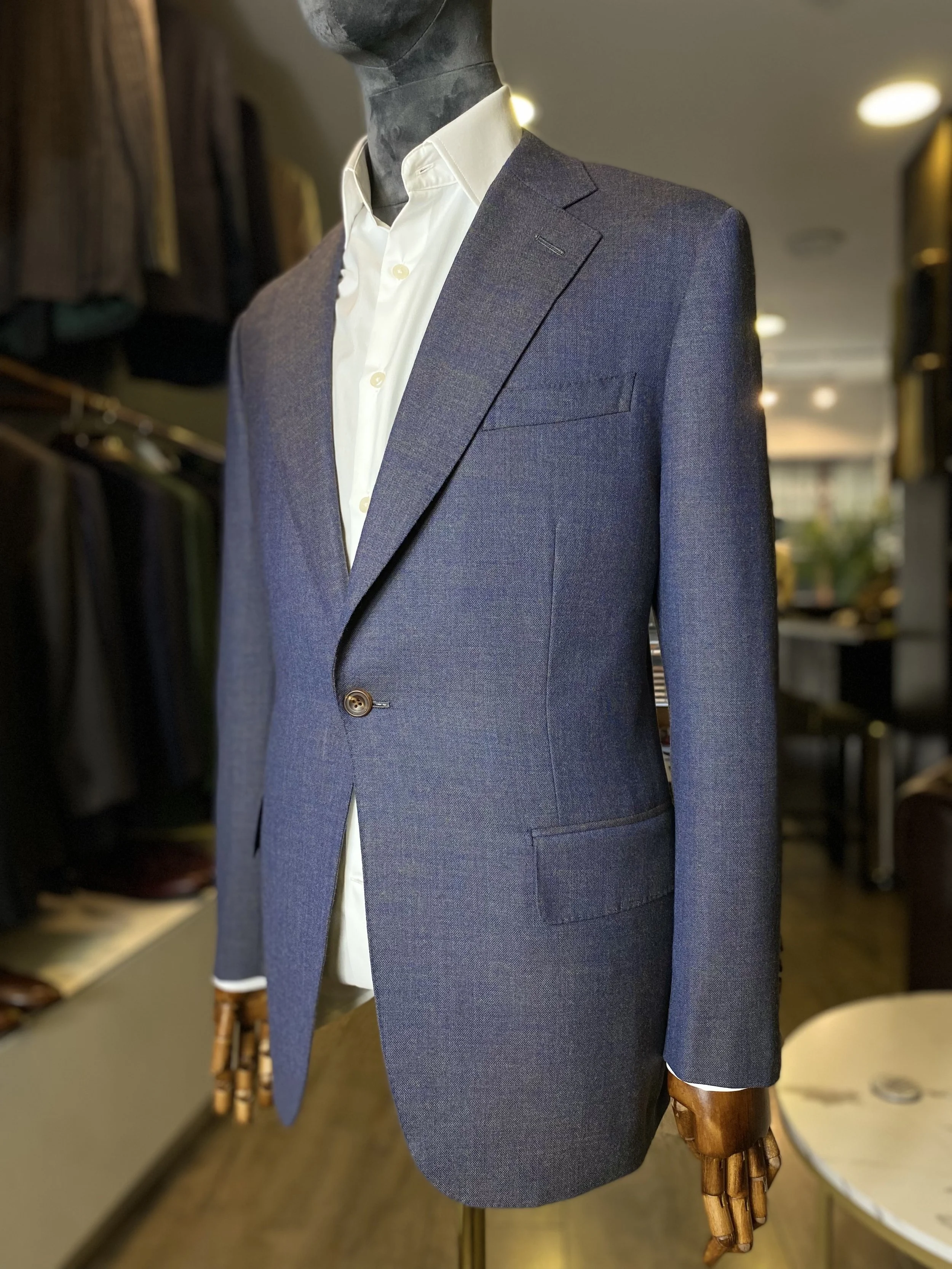 Blue/Grey Loro Piana High-twist Kale bespoke blazer. A sophisticated blue-grey one-button and slanted pockets blazer crafted from luxurious Loro Piana high twist wool, featuring elegant slanted pockets and a clean bespoke silhouette. Displayed on a s