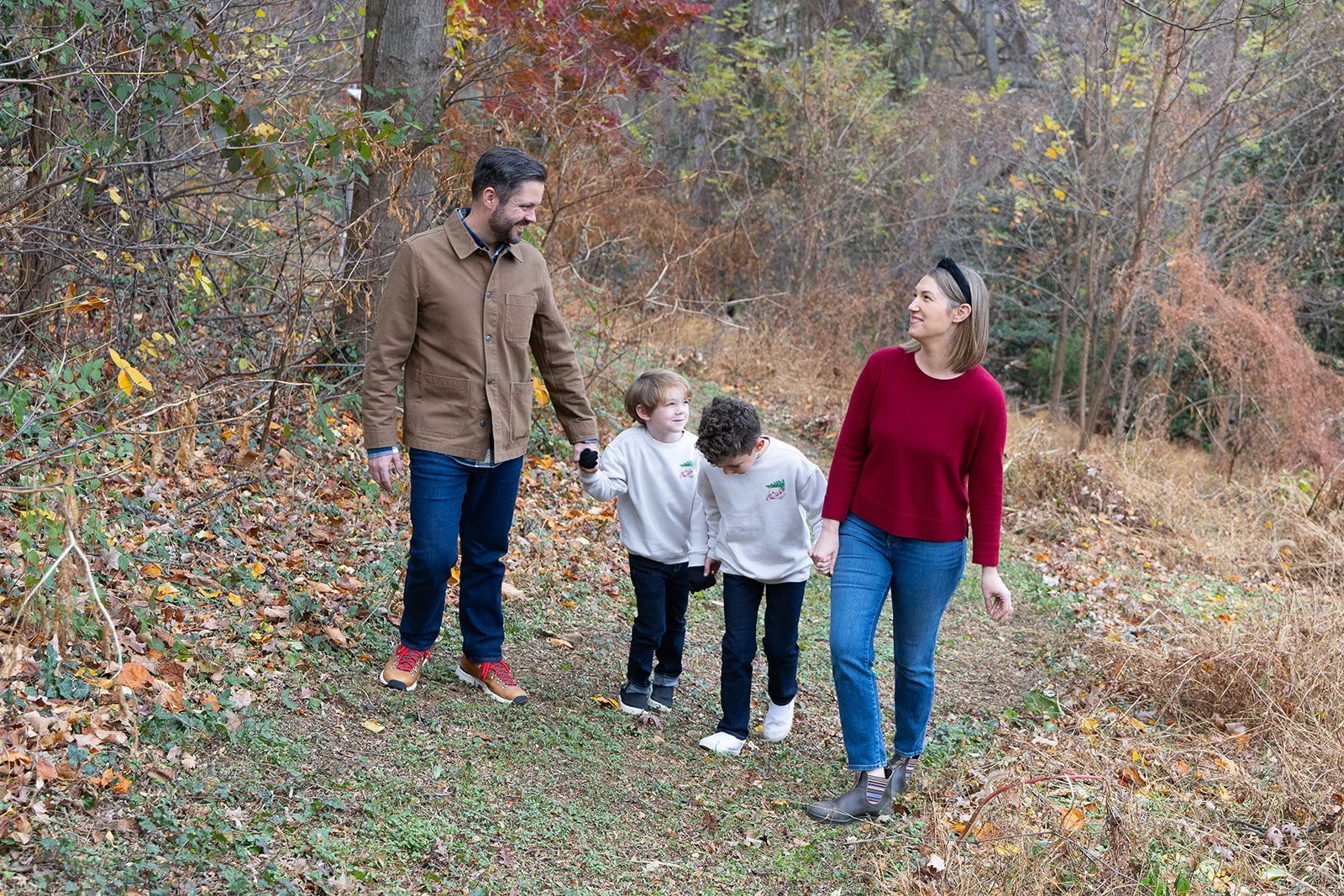 A family walking together on a forest trail in fall, holding hands and smiling.