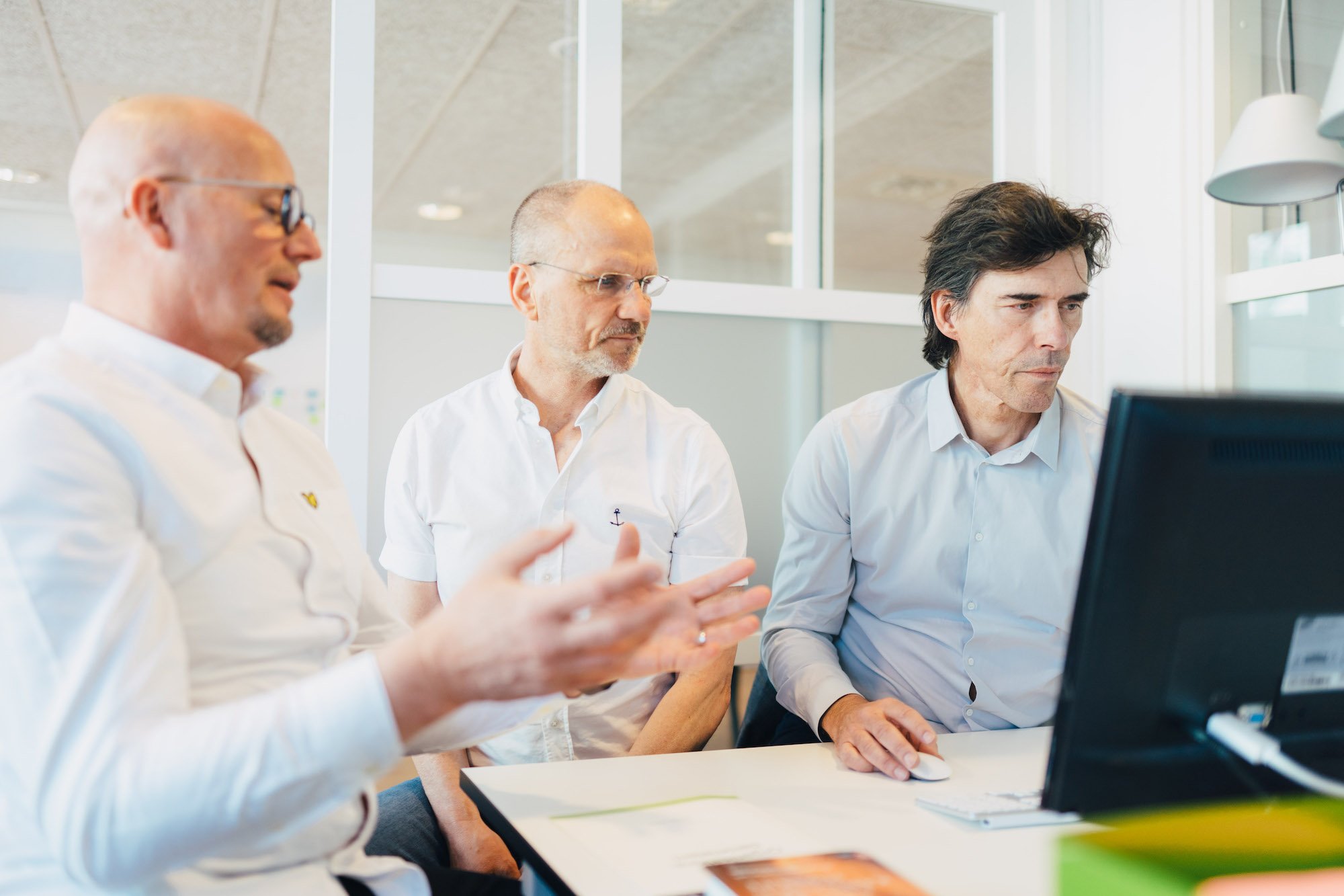 Tre män i vita skjortor som arbetar tillsammans vid ett skrivbord i ett modernt kontorsutrymme