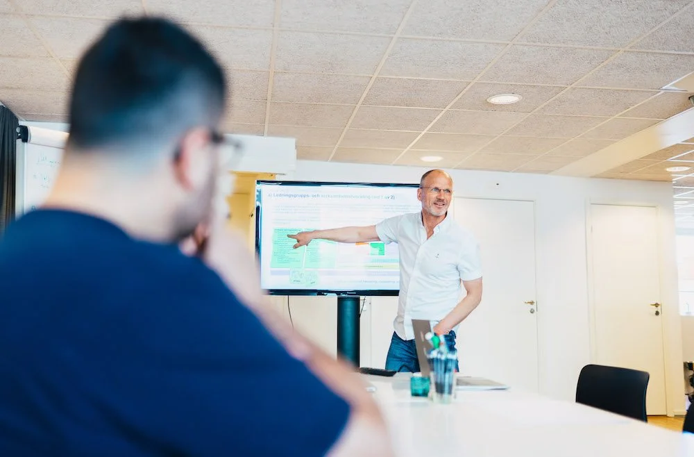 En man håller en presentation framför ett digitalt skärm i ett konferensrum medan en annan person tittar på.