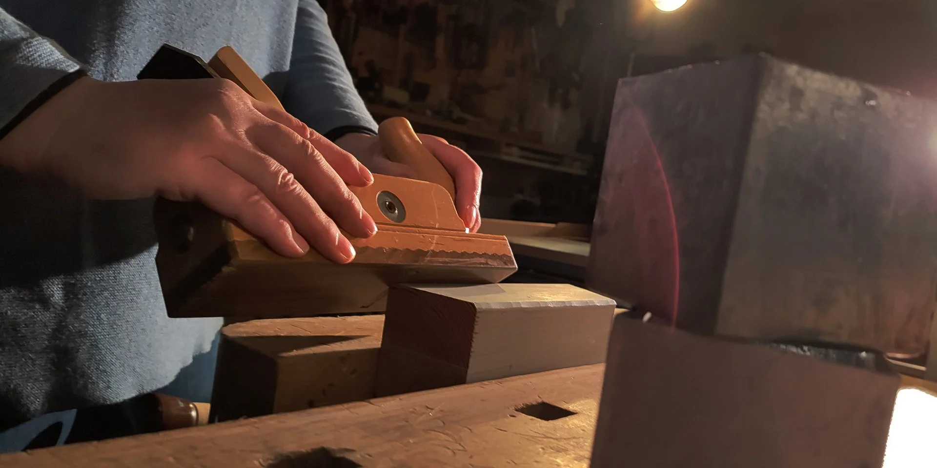 Person sägt Holz mit einer Handsäge in einer Werkstatt.