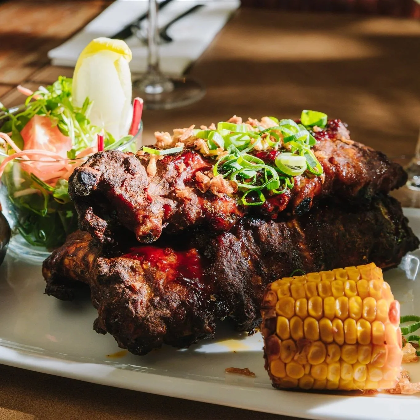 Grote barbecue-ribbetjes, geserveerd met maïskolf en salade.