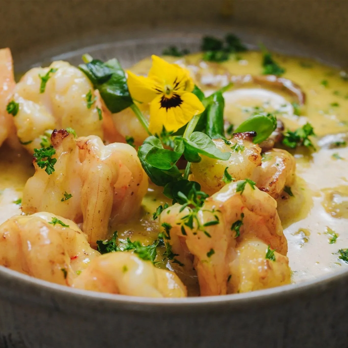 Scampi's in een gele currysaus met groene kruiden en een bloemetje als afwerking.