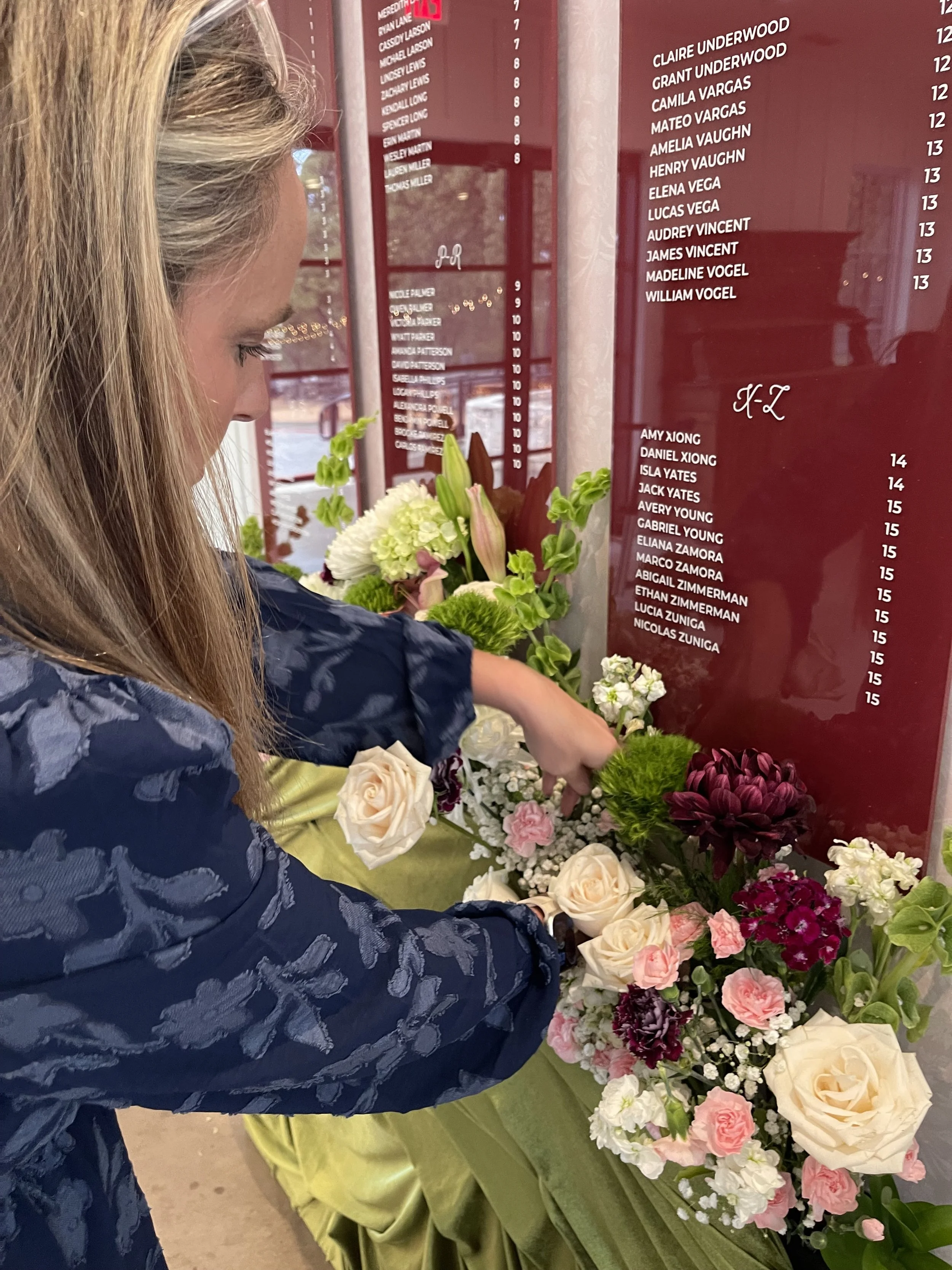 Behind the scenes with Covenant Design Co. as owner and designer Misty arranges lush florals in shades of burgundy, blush, and cream for a custom wedding seating chart installation at Bella Cavalli in Aubrey, Texas.