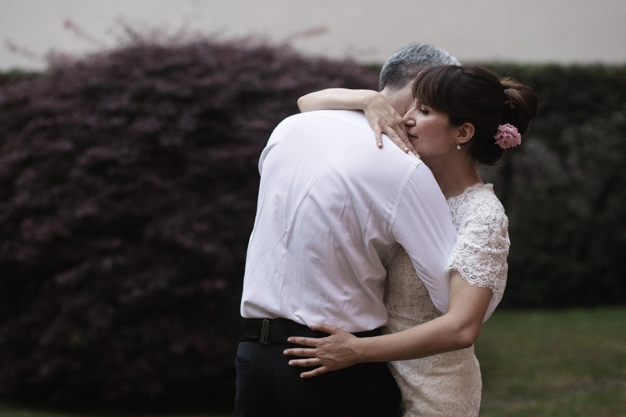 Una coppia di sposi si abbraccia e si bacia all'aperto, con sfondo di arbusti, durante un matrimonio.