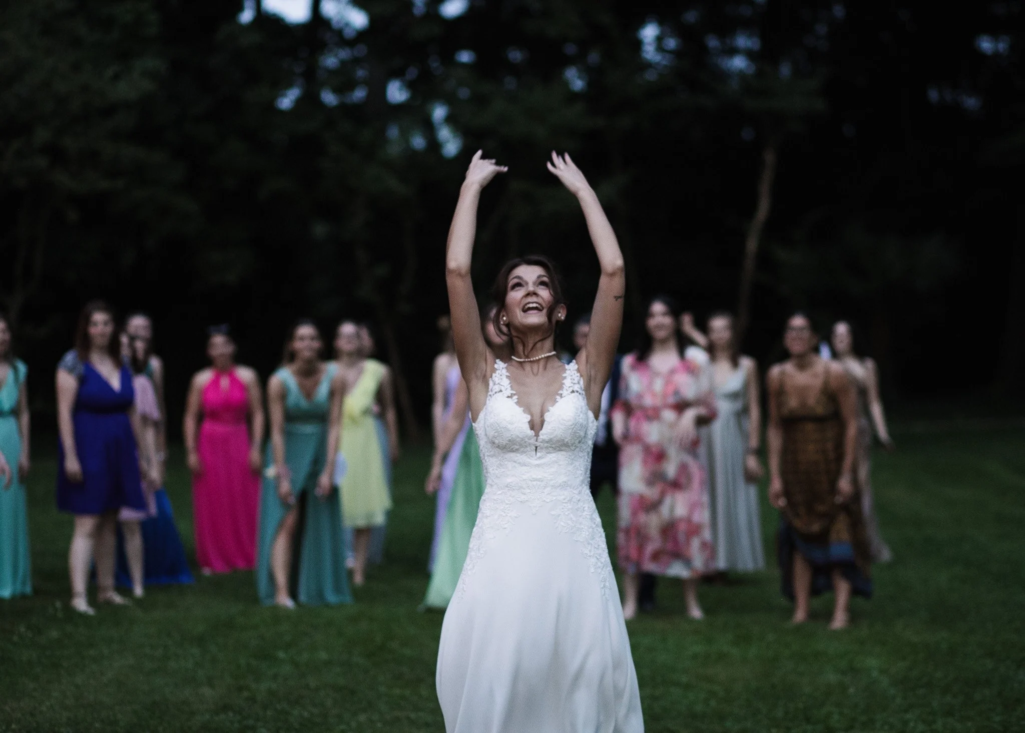 Una donna in abito da sposa che balla con le braccia sollevate davanti a un gruppo di persone in un giardino.