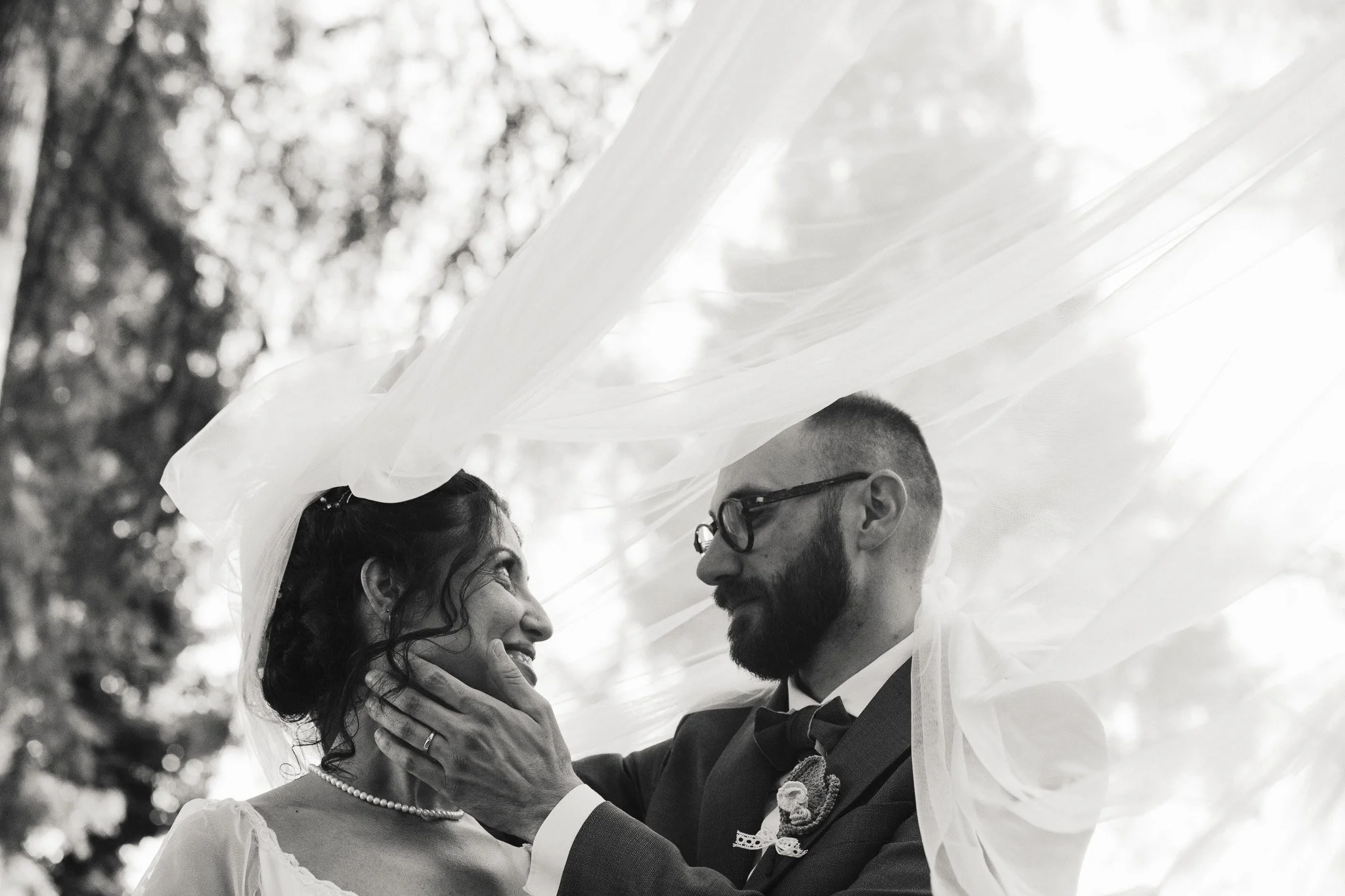 Un matrimonio su una cerimonia all'aperto, con la sposa e lo sposo che si guardano con affetto, sotto un velo di tulle trasparente.