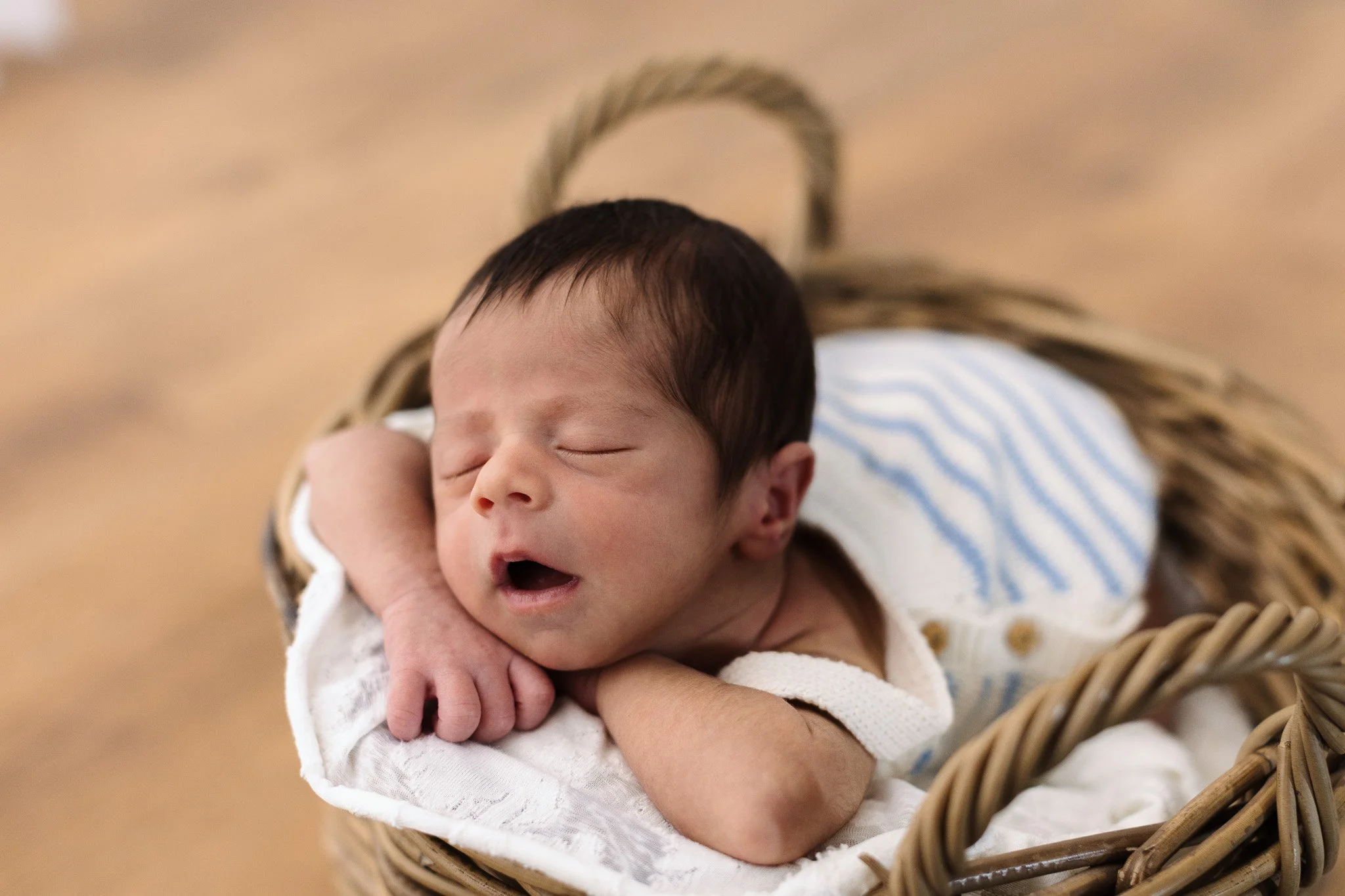 Neonato con capelli scuri, dorme in una cesta di vimini, poggiato sul suo braccio.