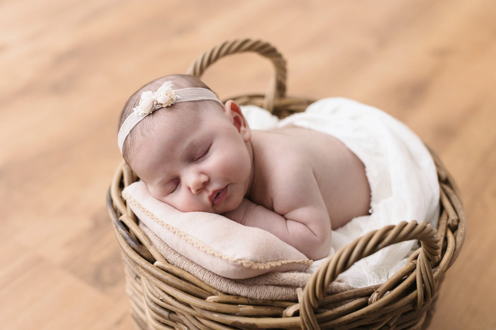 Bambino neonato addormentato in un cestino di vimini, con fascia decorativa in testa, cucce di stoffa e pavimento di legno