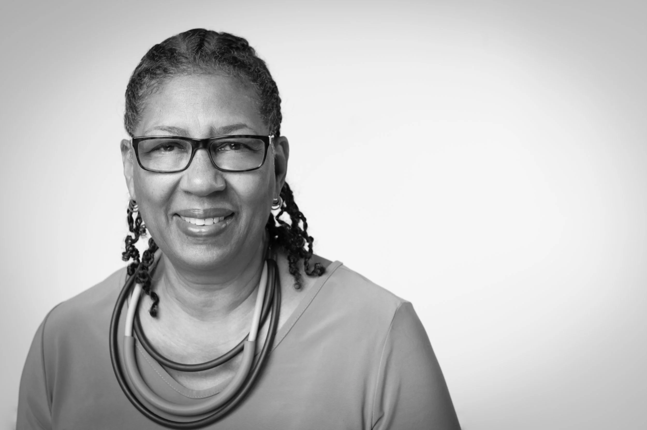 Black and white portrait of a smiling woman with glasses, braids, and a stethoscope around her neck.