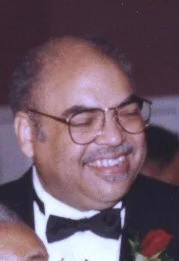 Smiling man wearing glasses, tuxedo, and bow tie.