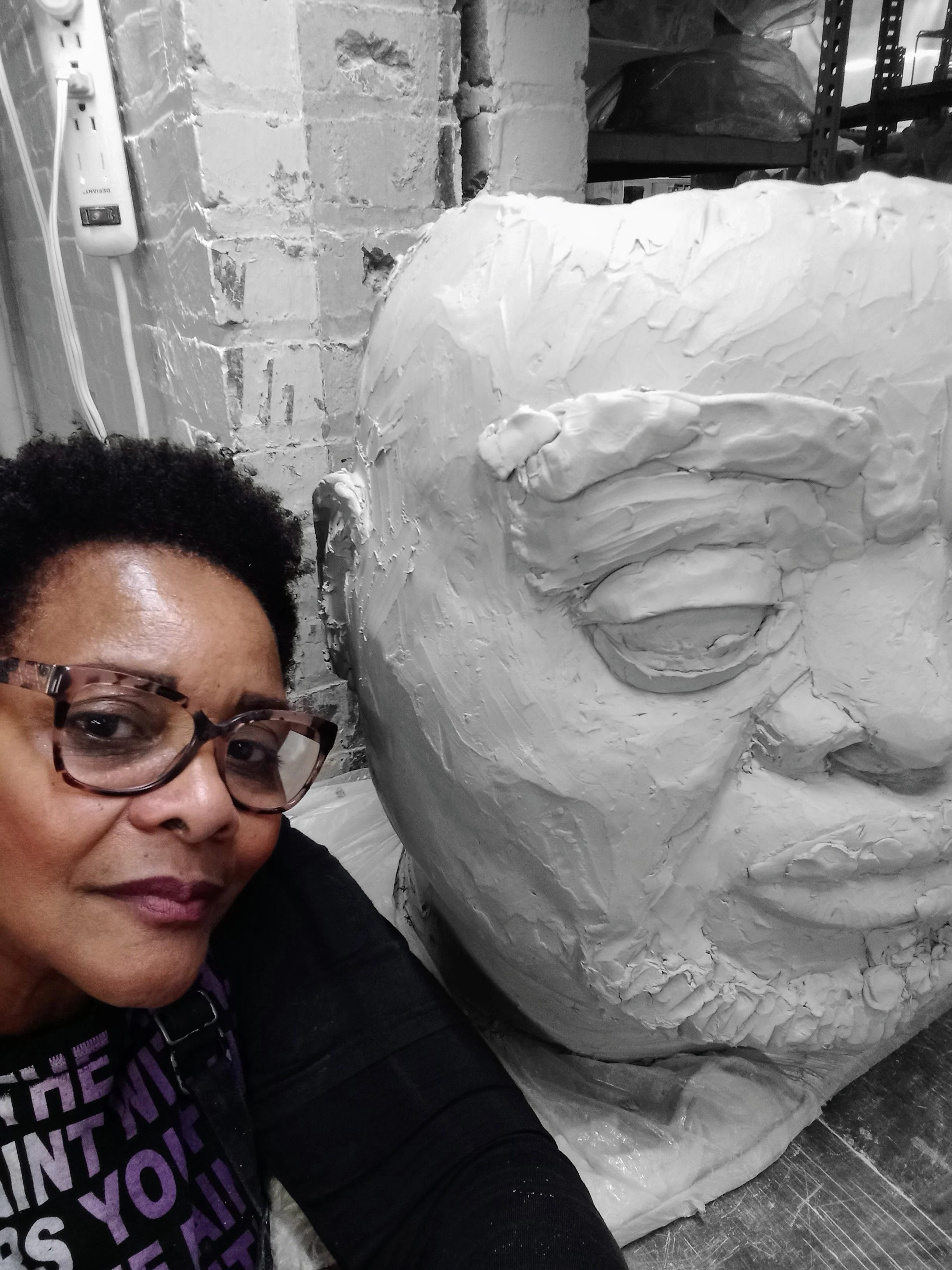 A color photo of Janathel Shaw, the artist posing by a portrait sculpture
