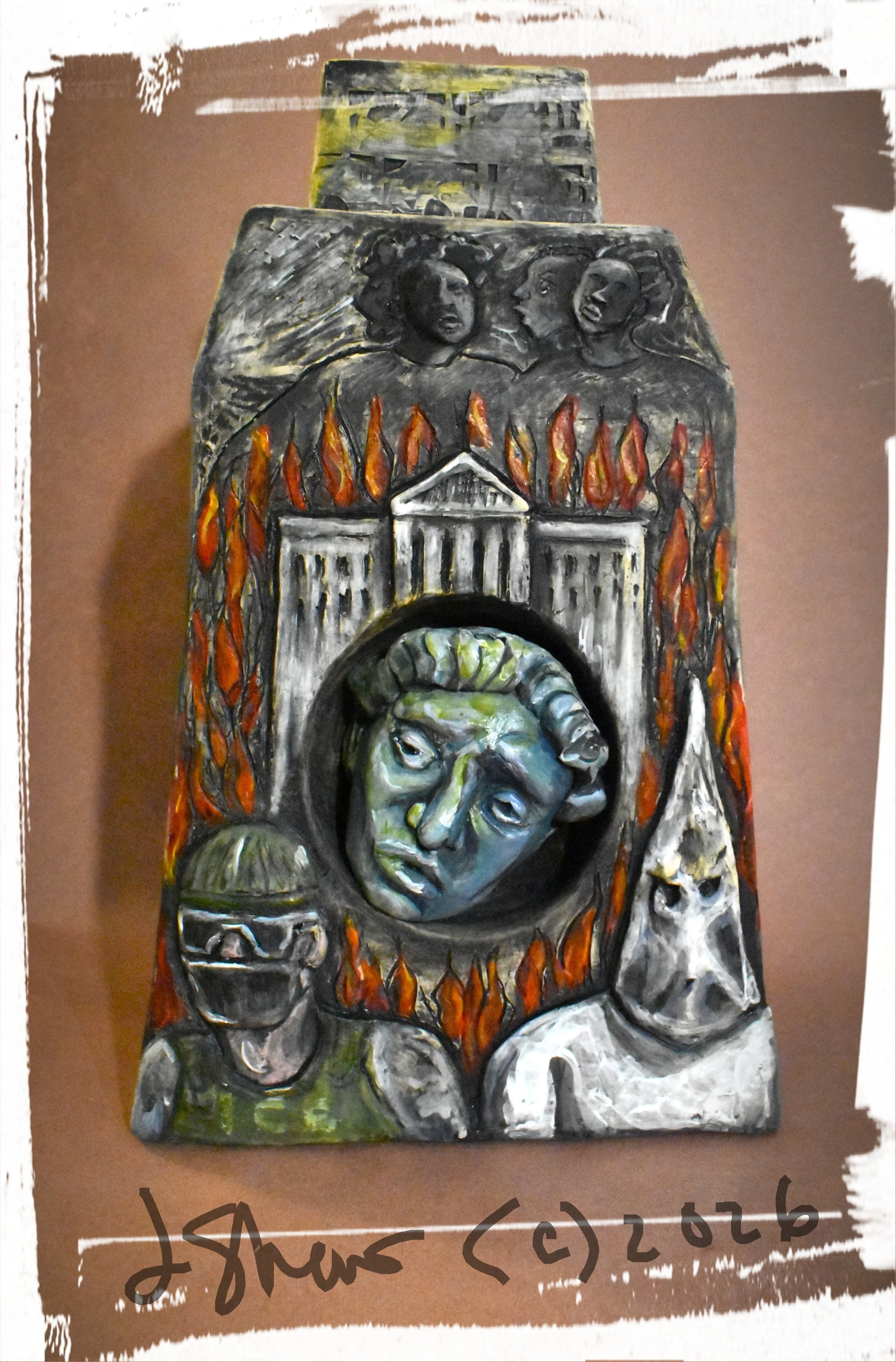 Colorful sculptue with a face in the middle with a face on either side with a building in the background