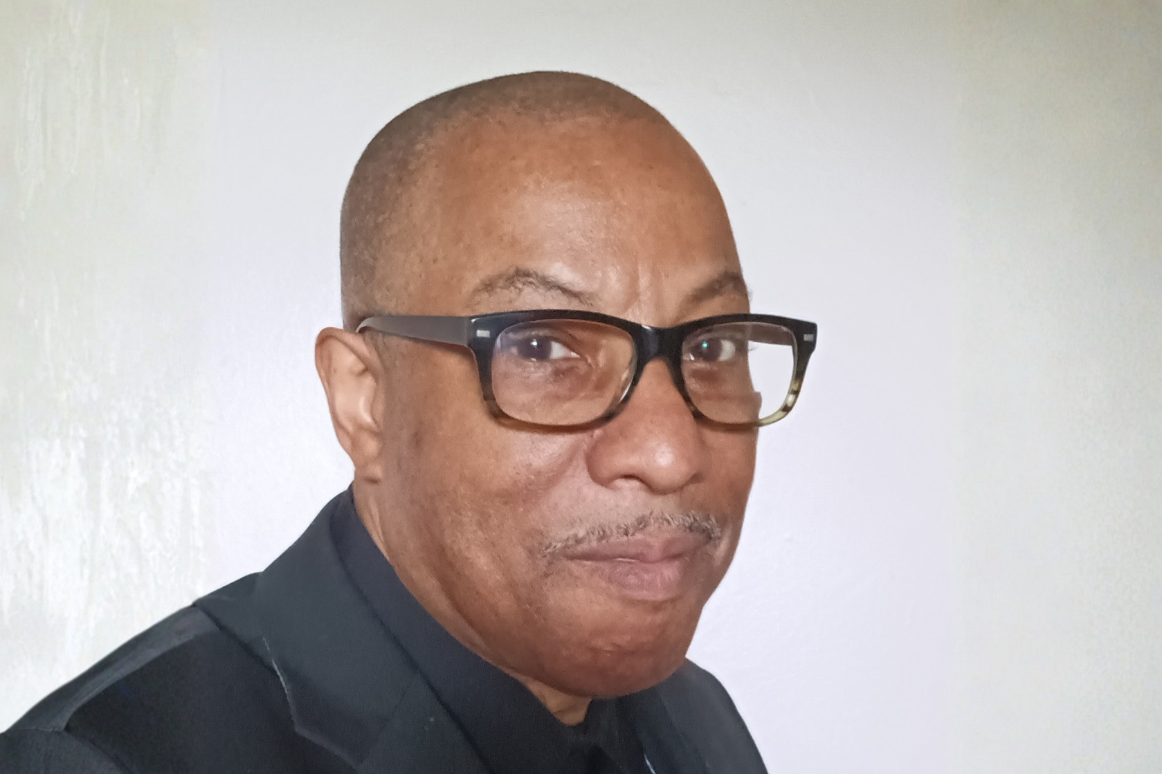 Man with glasses dressed in a black shirt and coat 