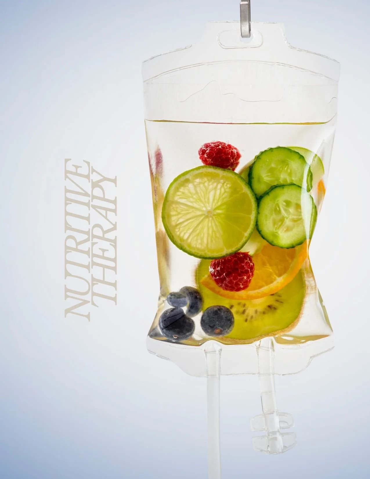A medical IV drip bag filled with water and fresh fruit slices, including lemon, cucumber, raspberry, blueberry, mango, and orange, with the words "NUTRITION THERAPY" written beside it.
