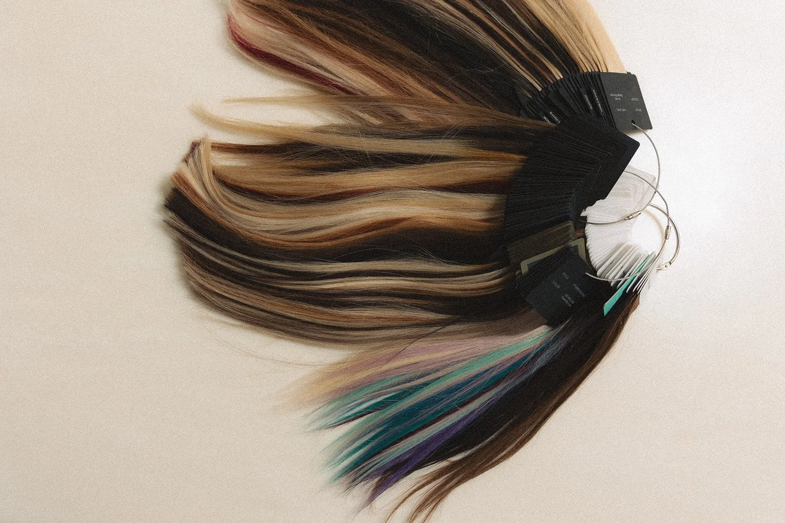 A collection of hair extension color samples arranged on a surface, varying from blonde to dark brown with some sections dyed in pastel colors like teal and purple.