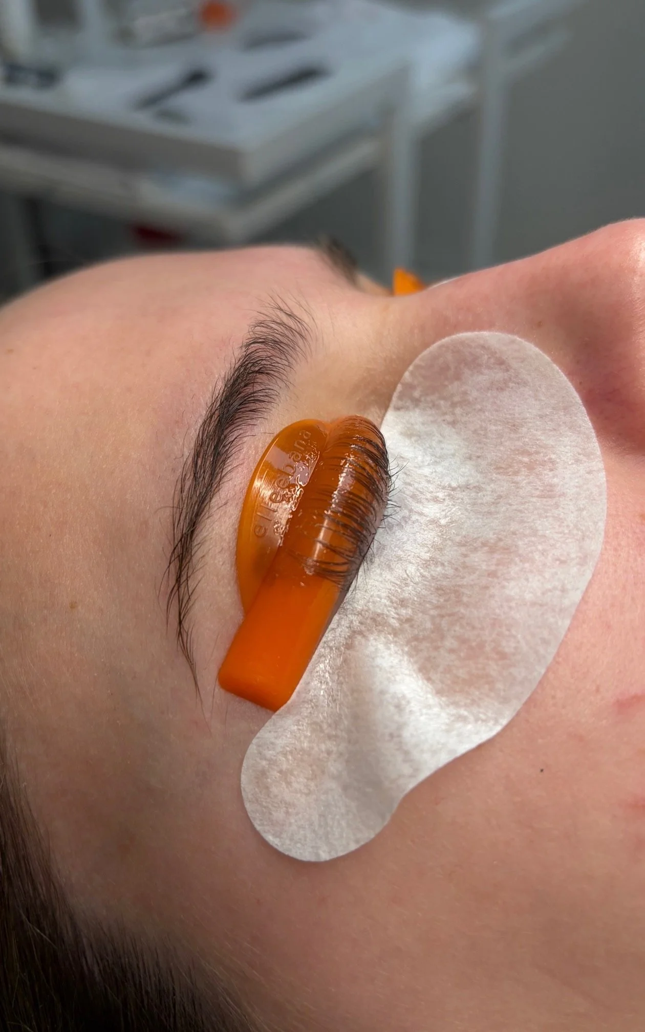 A person receiving Lash lift and tint with adhesive pad under eye, relaxed in a beauty clinic.