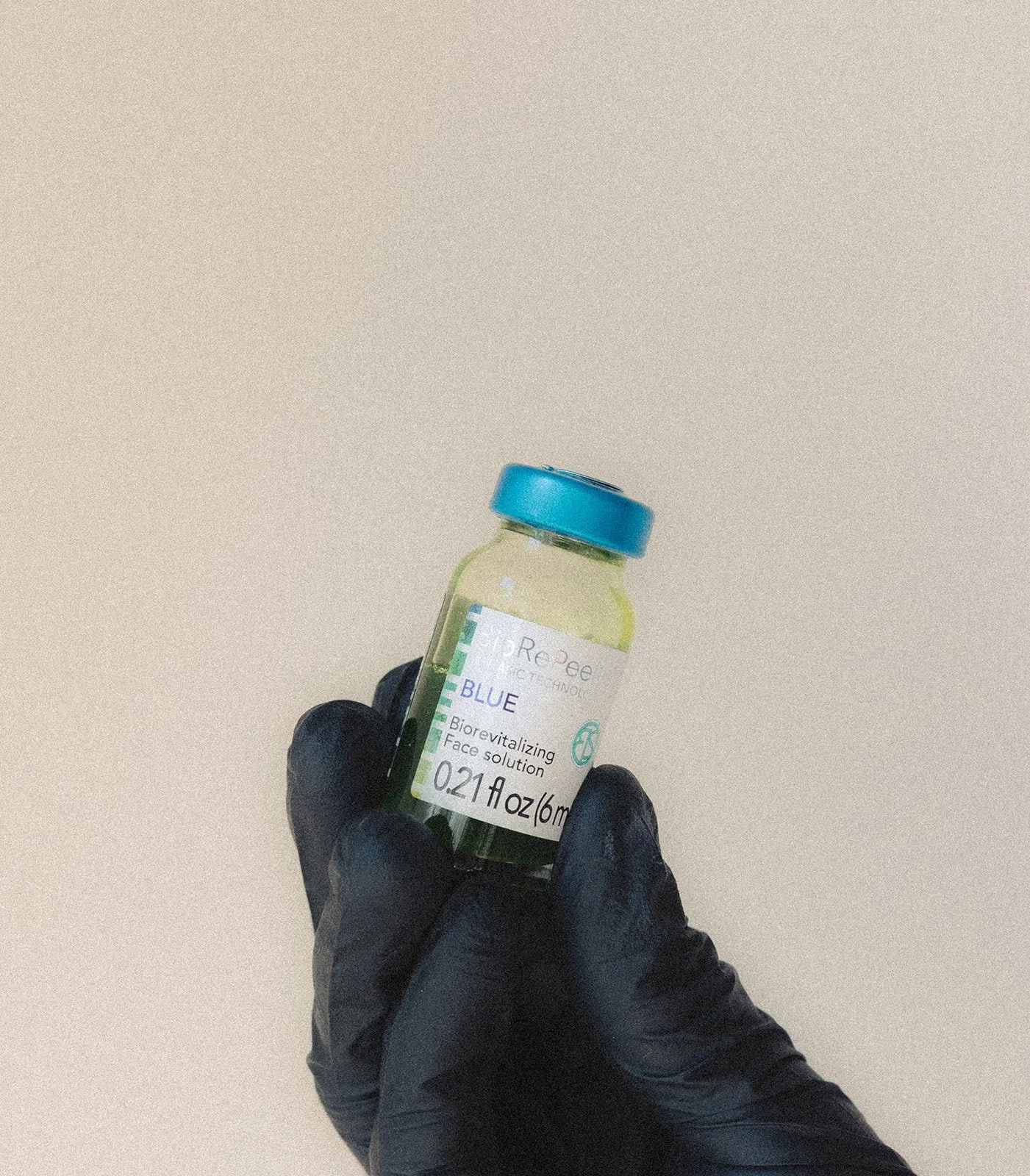 A hand wearing a black glove holding a small vial labeled 'Biorevitalizing Face Solution' with a blue cap and white label.