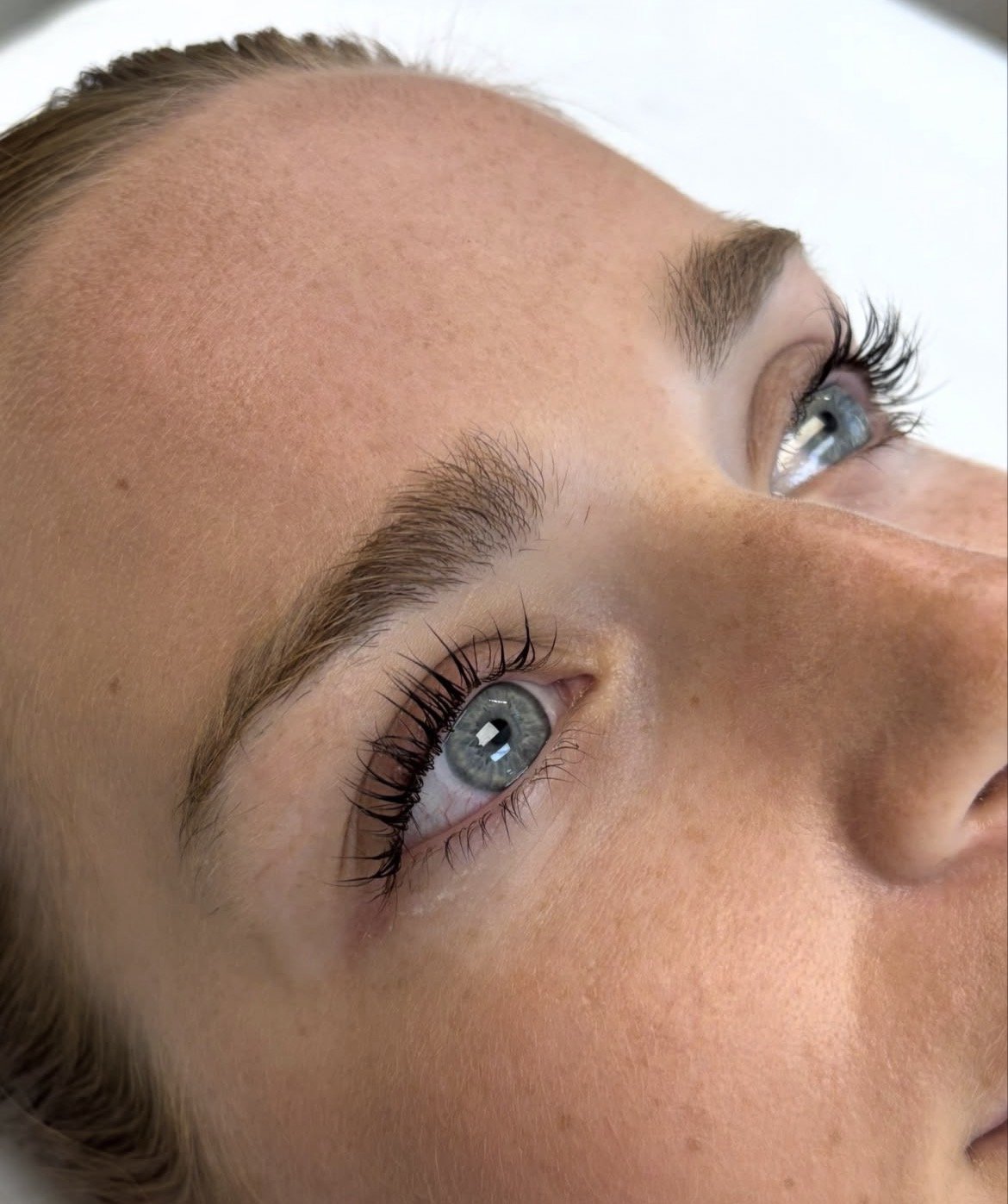 Close-up of a woman’s face, focusing on her blue eyes, eyebrows, and a portion of her forehead and nose.