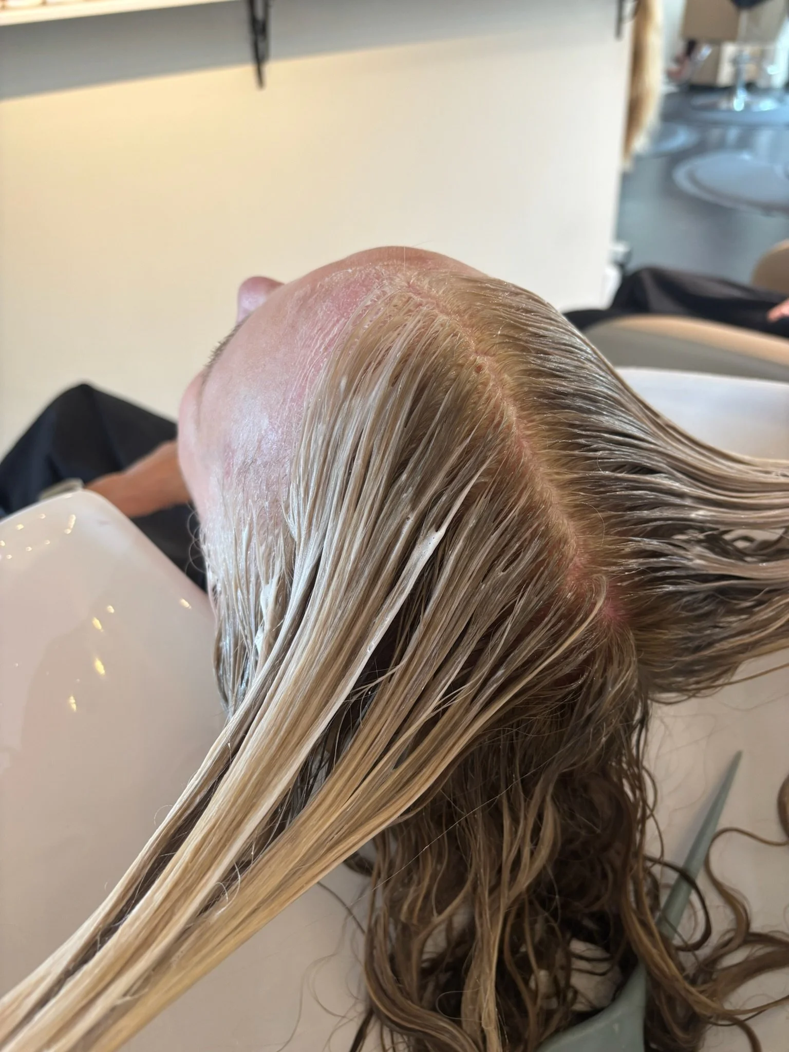 Person receiving a hair mask treatment at a salon, laying back with wet blonde hair.