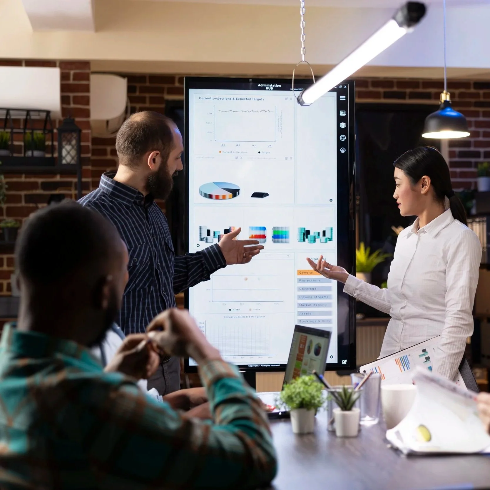 Group of people having a business meeting in a modern office, focused on a woman presenting data on a large digital display screen.