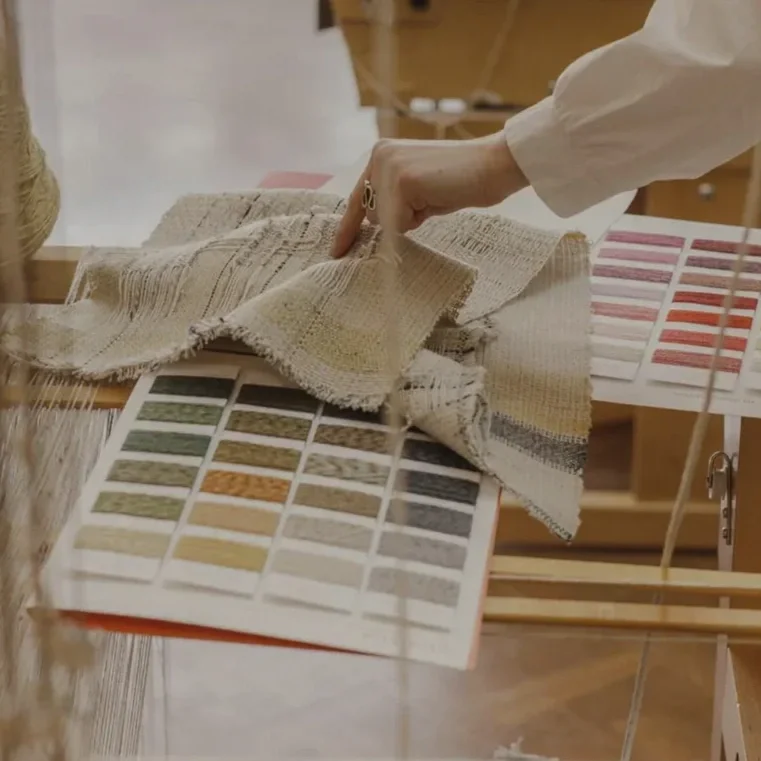 Person examining fabric samples and color swatches on a table.