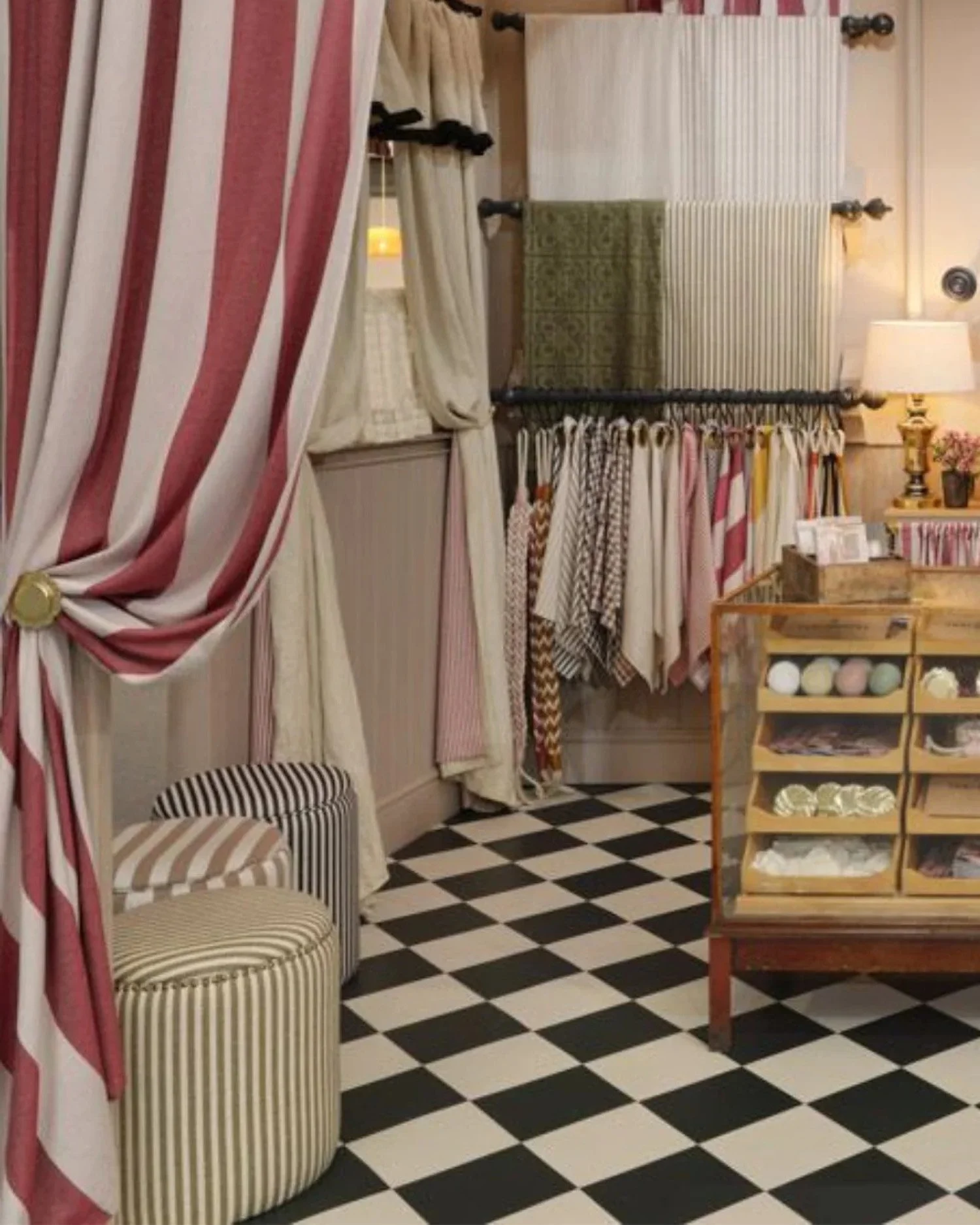 Inside a shop or boutique with black and white checkered floor, striped armchairs, curtain dividers, and a display shelf with linens or napkins.