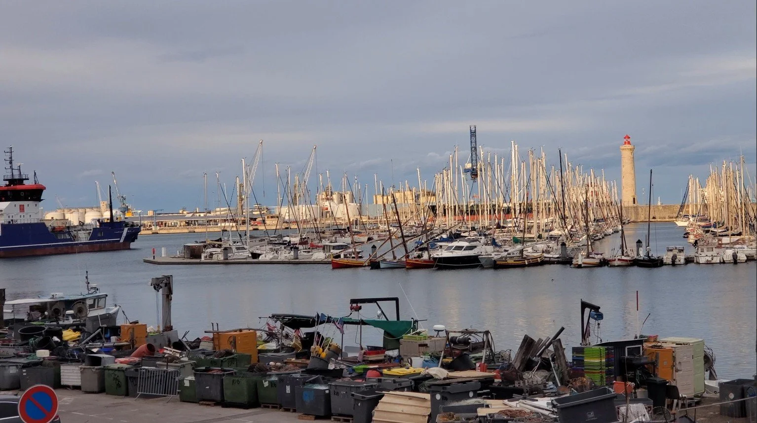 Sète working fishing port — boats, gear, and lighthouse in the background
