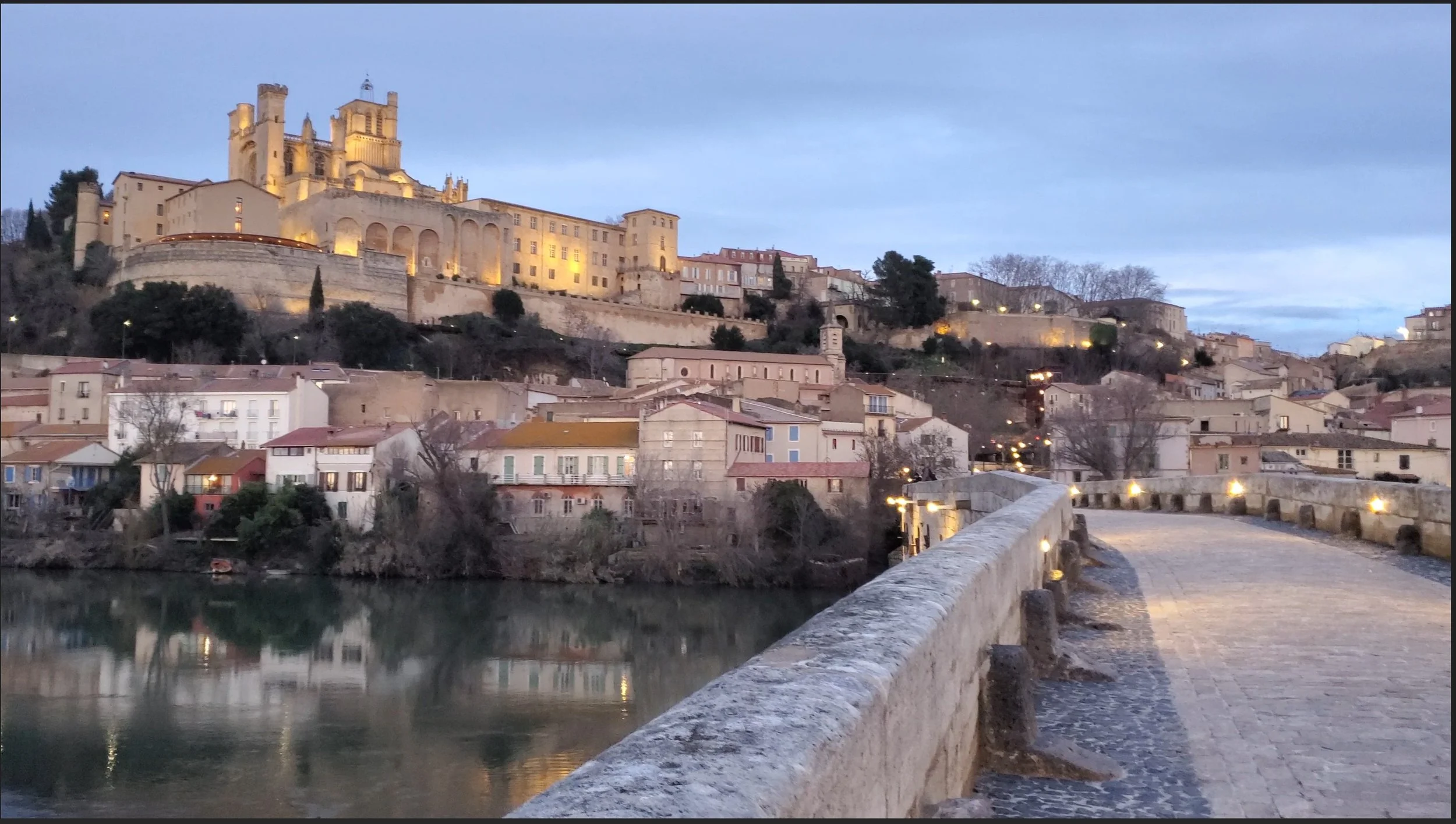 Béziers cathedral lit at dusk, viewed from the Pont Vieux over the Orb River