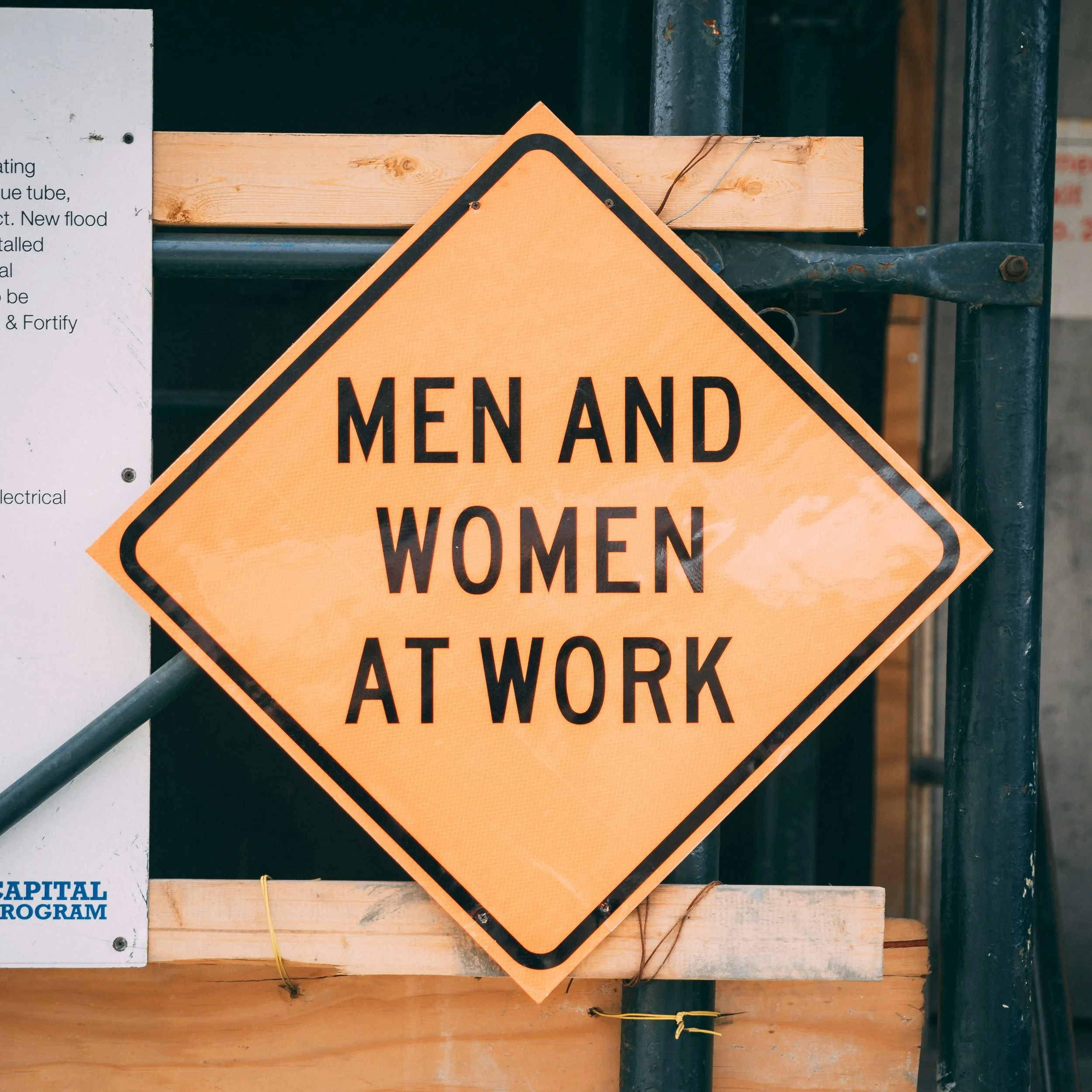 Un panneau orange avec écrit en anglais "Men and Women at Work".
