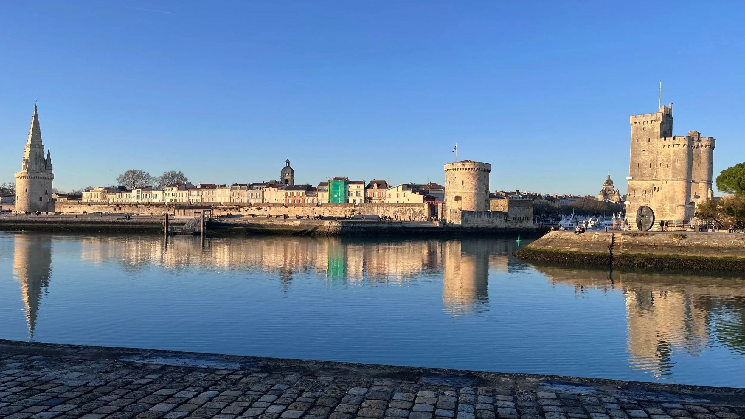 Vue du port de La Rochelle avec ses tours, le front de mer, et des bâtiments historiques sous un ciel clair.