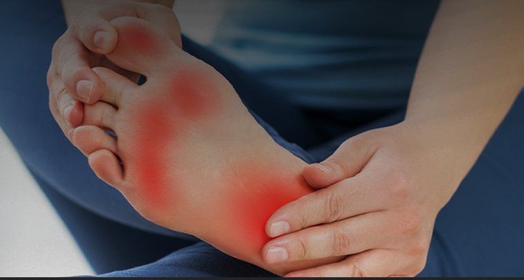 Person holding their foot with redness and pain near the heel, indicating possible injury or inflammation.