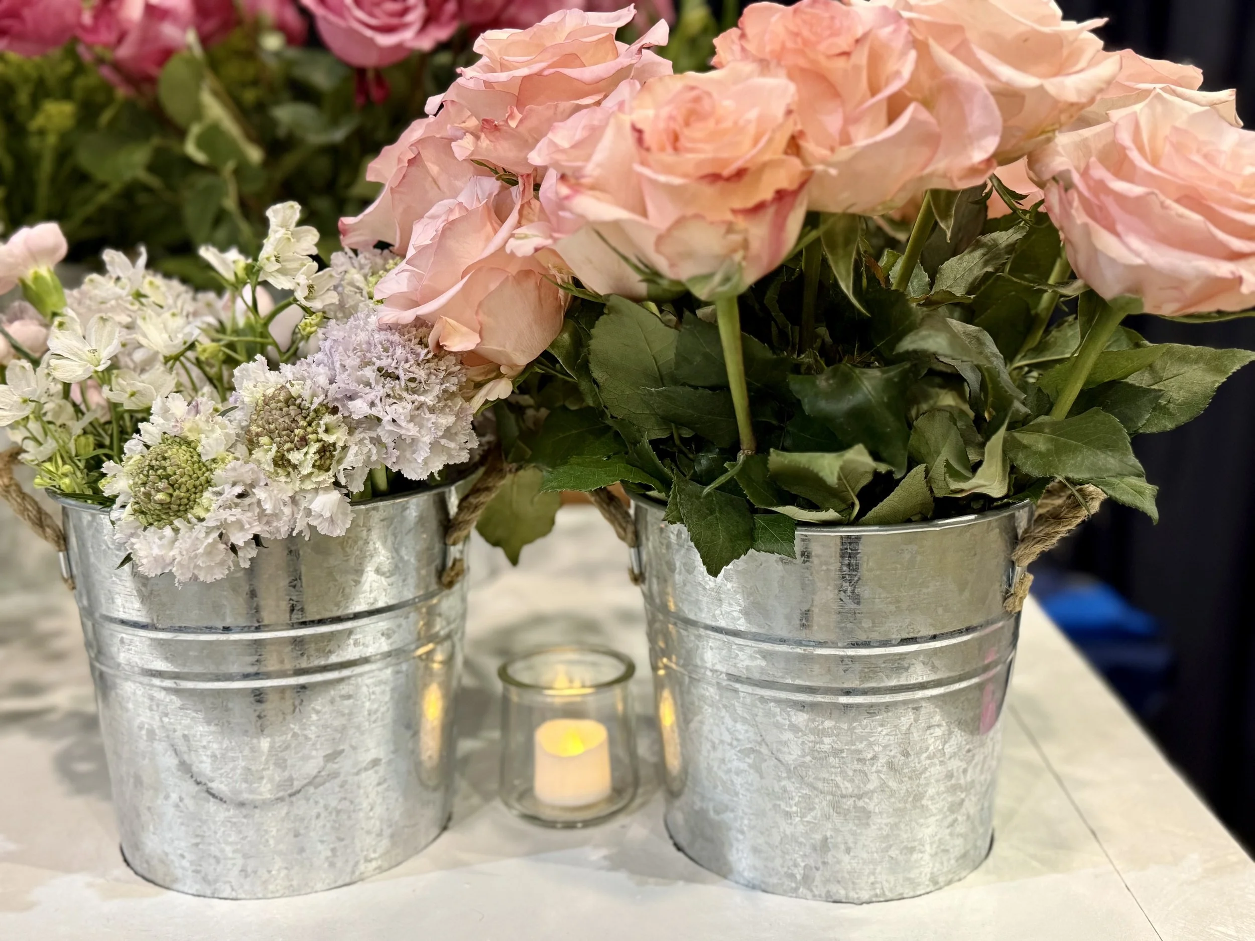 Close up of a flower cart with two metal buckets filled with pink roses and white flowers. We will work with you to choose flowers matching the season and your wedding theme.