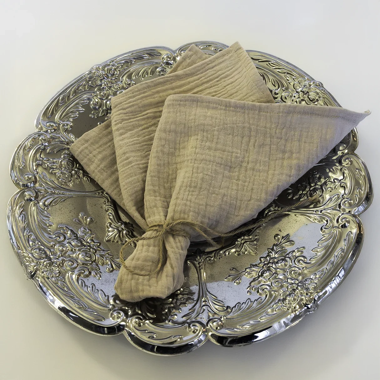 Beige pellavaservetti hopeoidulla tarjottimella JuhlaToppilan astiavuokrauksessa.