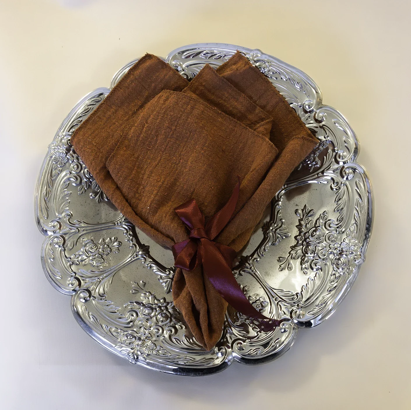 Oranssi pellavaservetti hopeoidulla tarjottimella JuhlaToppilan astiavuokrauksessa.