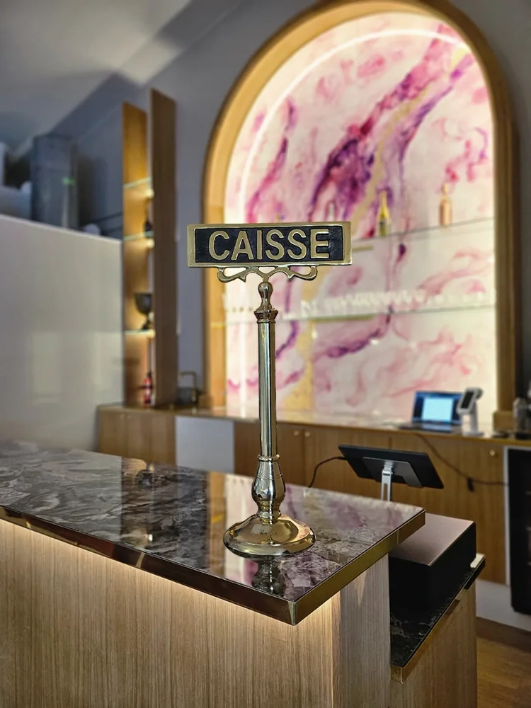 Juhlatilan baaritiski, jossa marmoria muistuttava taso, Caisse-kyltti ja taustalla valaistu kaariseinä hyllyineen, tila myös mahdollistaa omat juomat juhlatilassa.