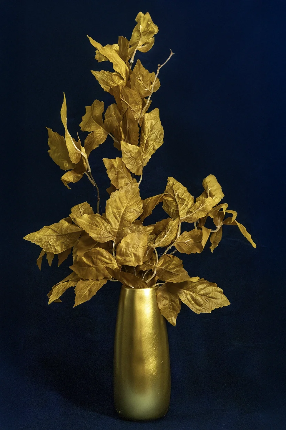 Kultainen korkea maljakko, jossa on keltainen silkkivaahteranlehtioksa JuhlaToppilan somistevuokrauksessa.