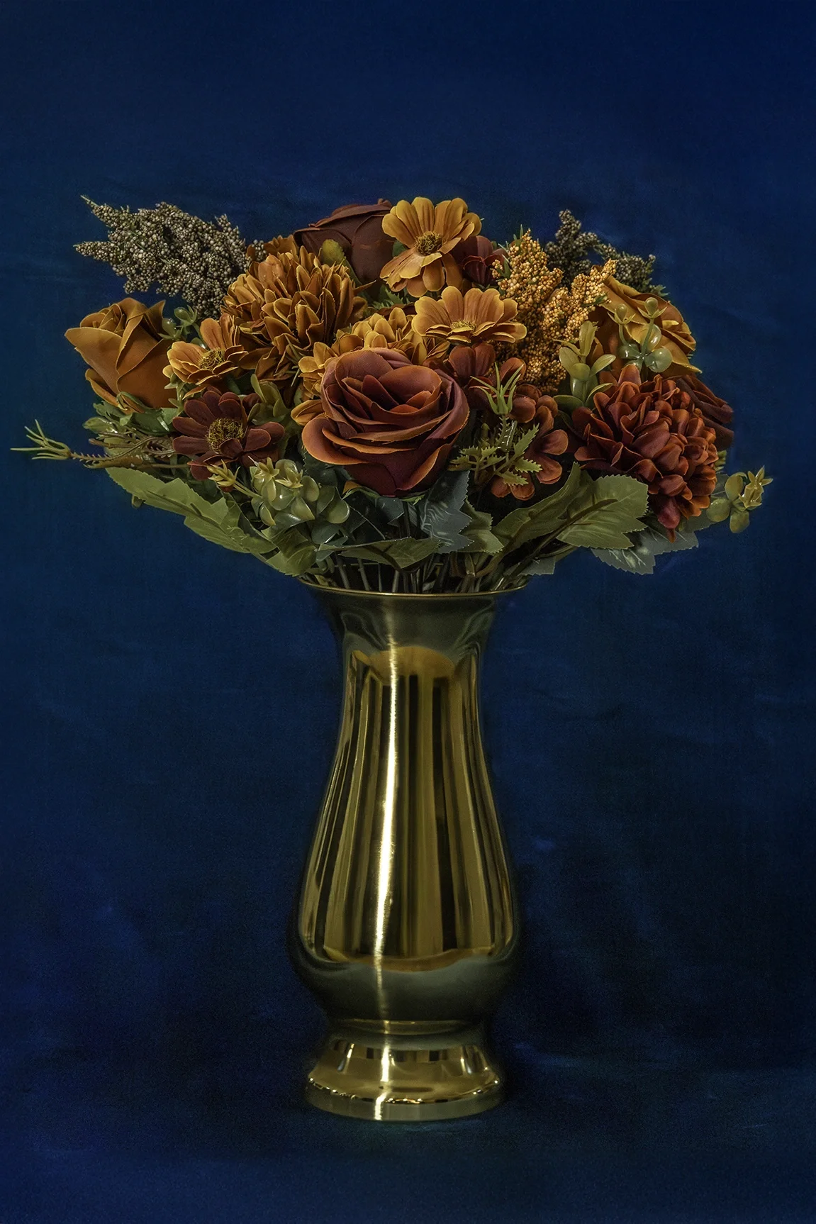 Kultainen metallimaljakko, jossa on oranssi-punainen silkkikukkakimppu JuhlaToppilan somistevuokrauksessa.