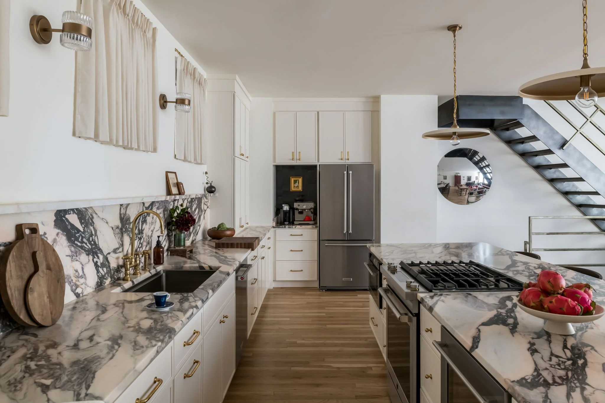 Cream kitchen with bold veined marble countertops and backsplash, brass fixtures, built-in coffee niche, stainless French door refrigerator, and professional gas range.